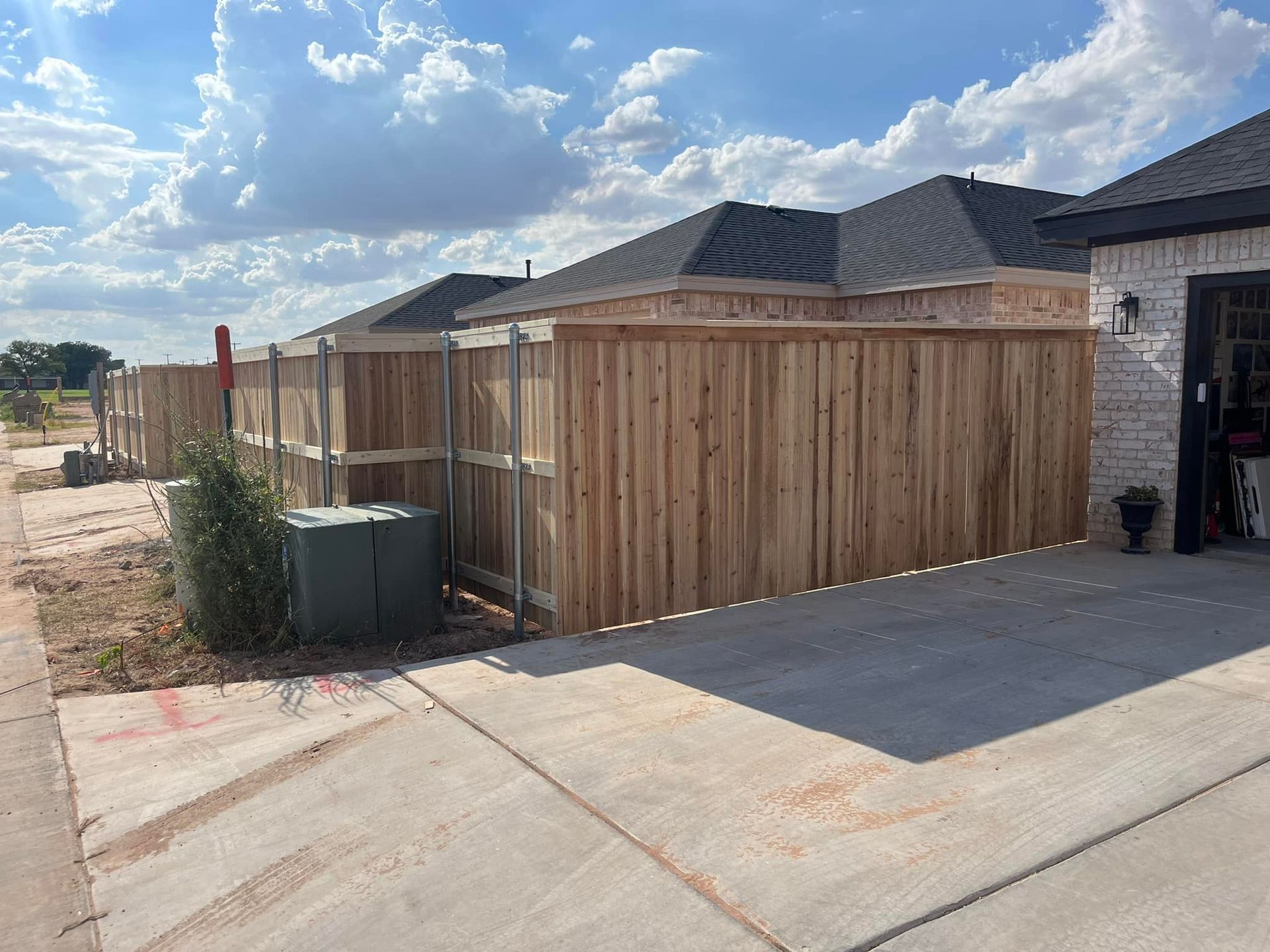 Wooden privacy fence along the side of a house and driveway under a cloudy sky.
