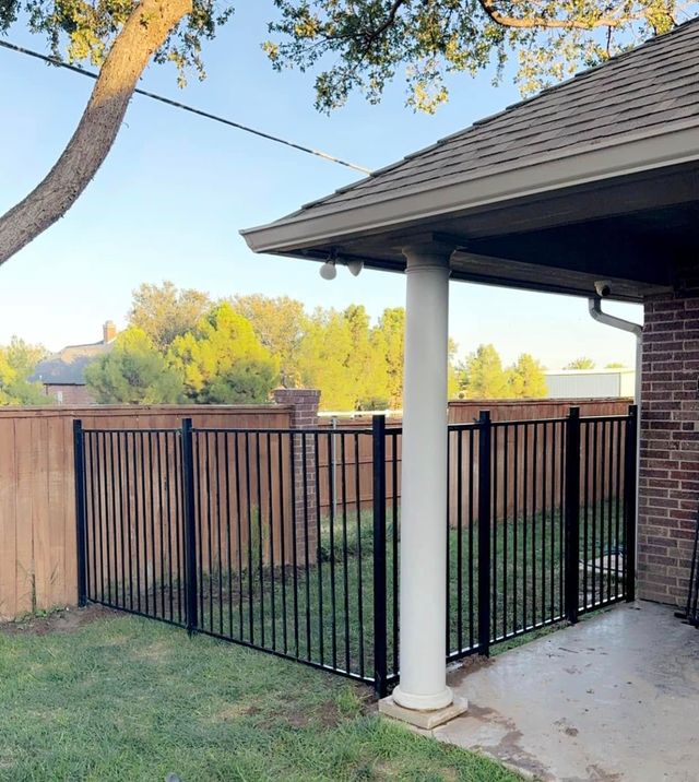 Black metal fence encloses a patio area next to a brick wall and a wooden fence.