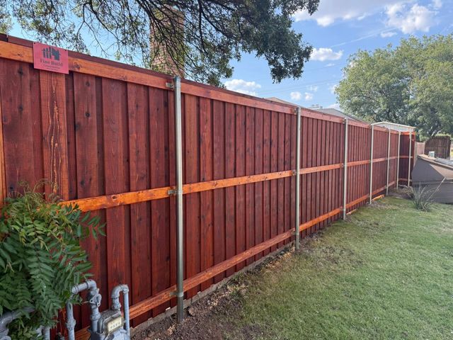 Red stained wooden privacy fence with metal posts in a yard.