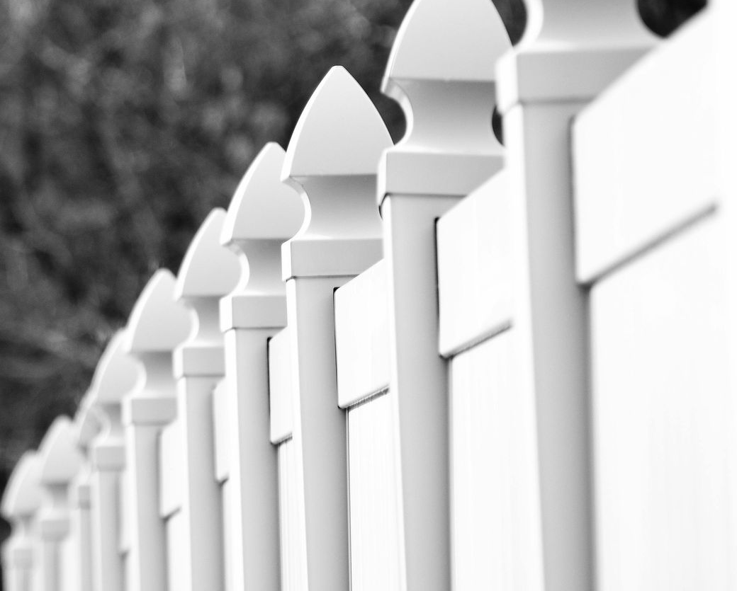 White picket fence, close-up, in a row, with pointed finials, blurred background.