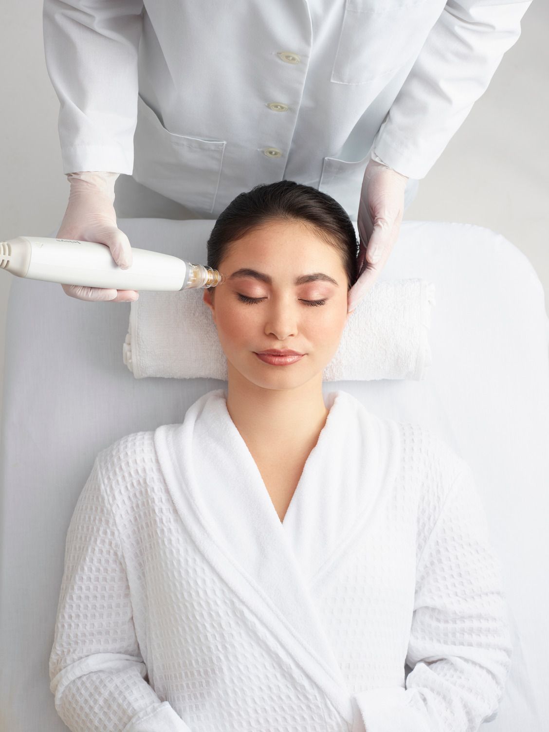 Woman receiving facial treatment in a clinic; medical professional using a device on her face.
