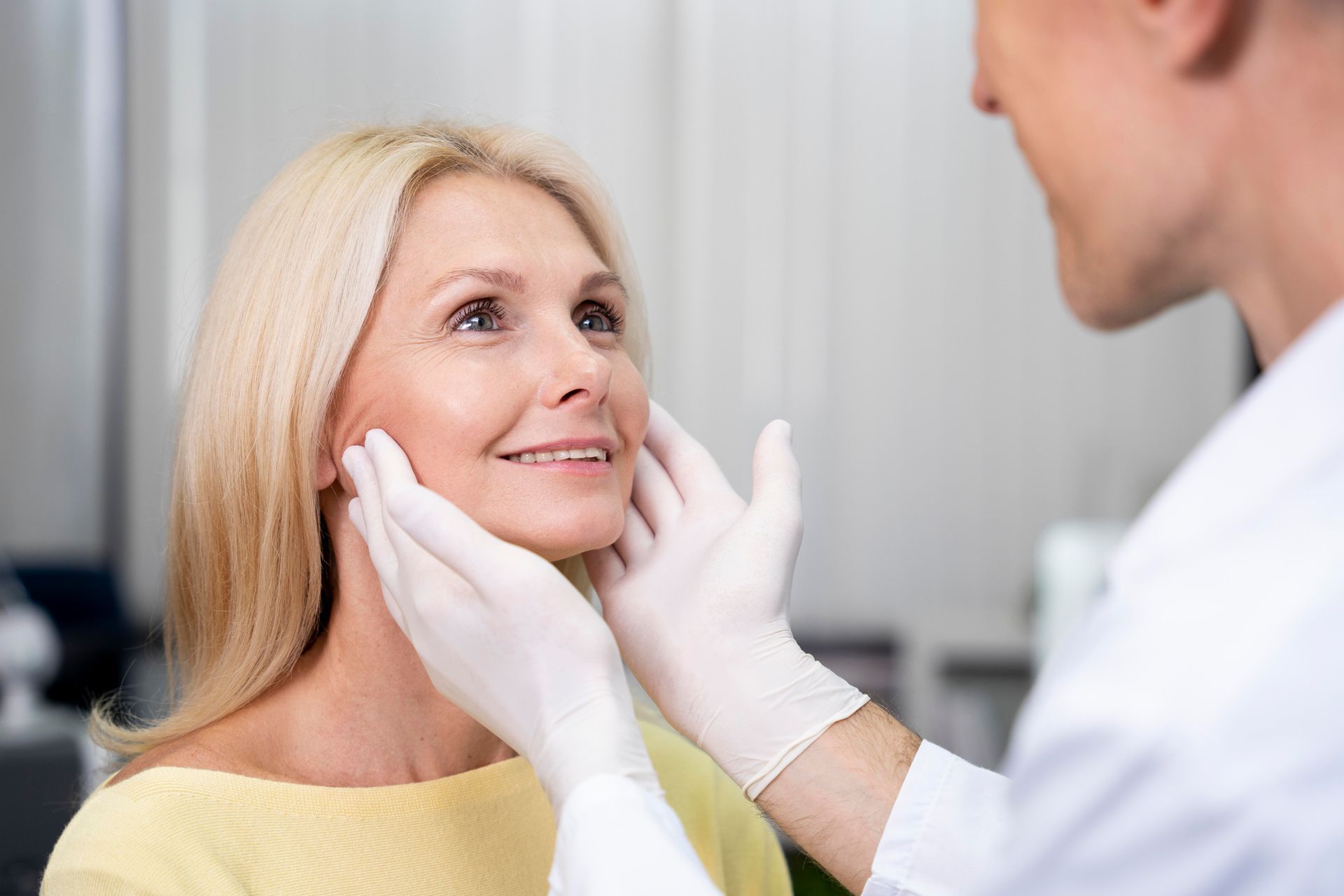 Doctor examining a person's face. Both smiling. The doctor wears gloves. Setting appears to be a medical office.