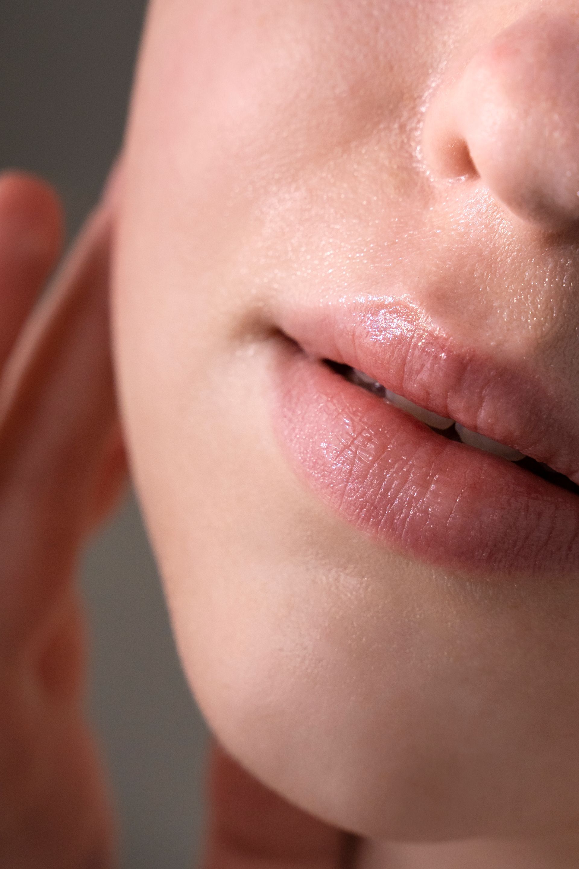 Close-up of a person's face; lips are slightly parted, glossy with pink lip product; skin is smooth.