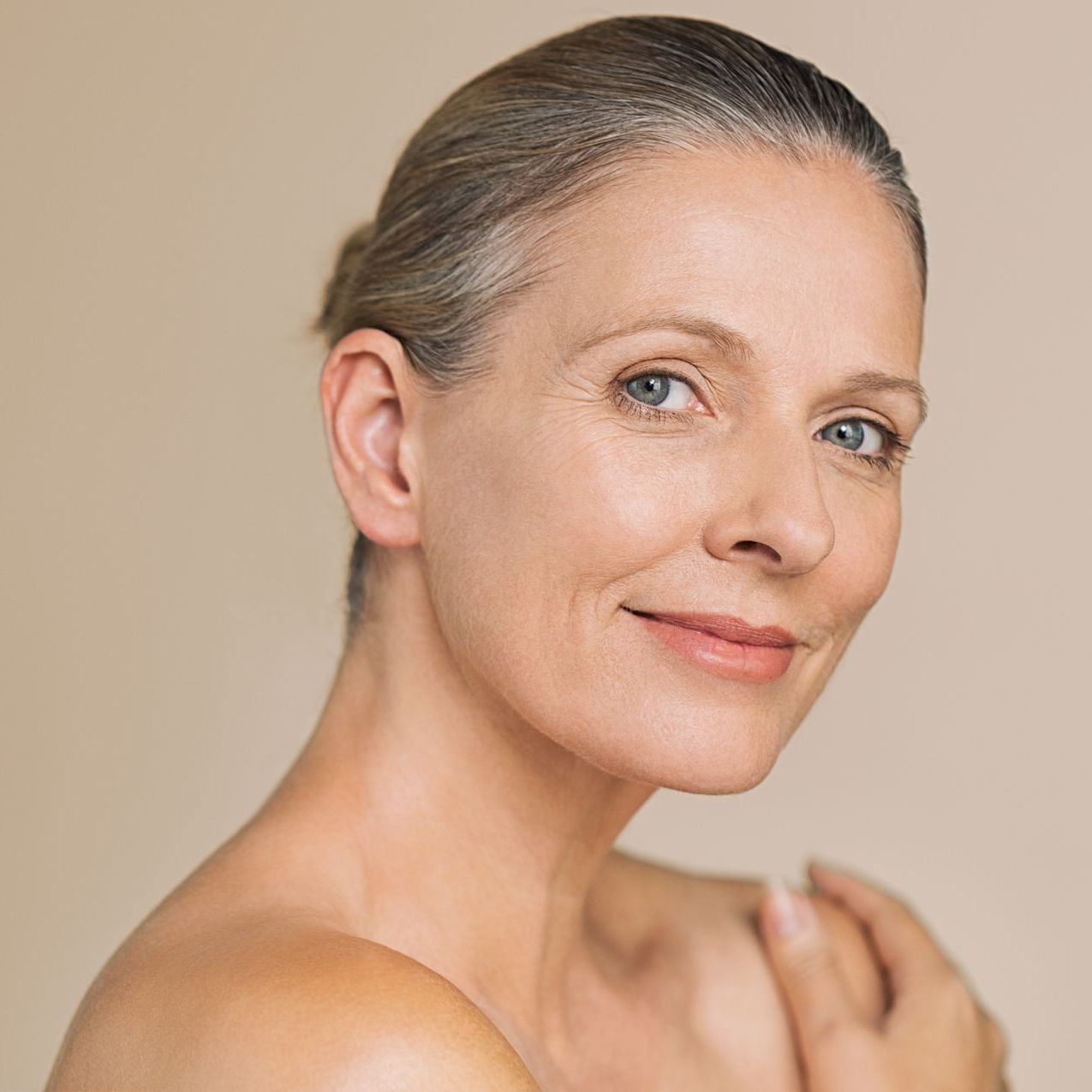 Woman with gray hair, smiling, bare shoulders, soft lighting.