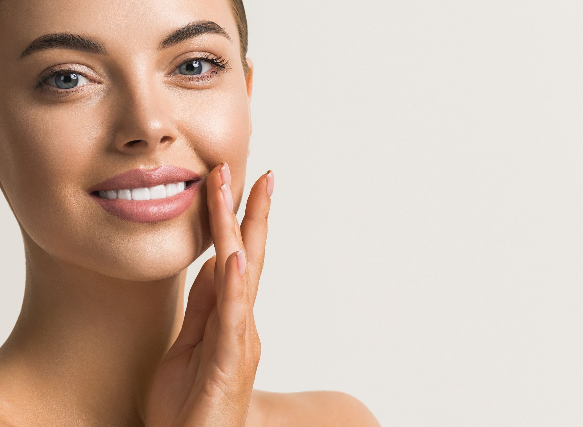 Woman with flawless skin smiling, touching her face with fingers.