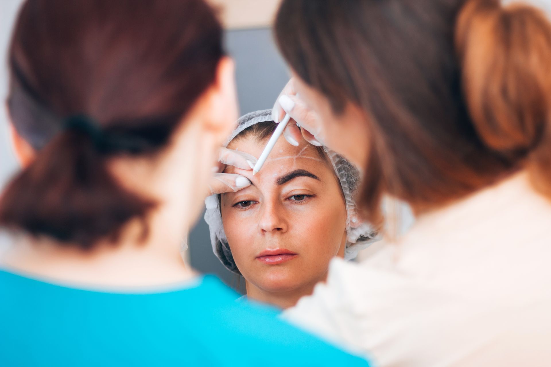 Woman having her eyebrow shape marked by esthetician with tools. Another person stands beside her.