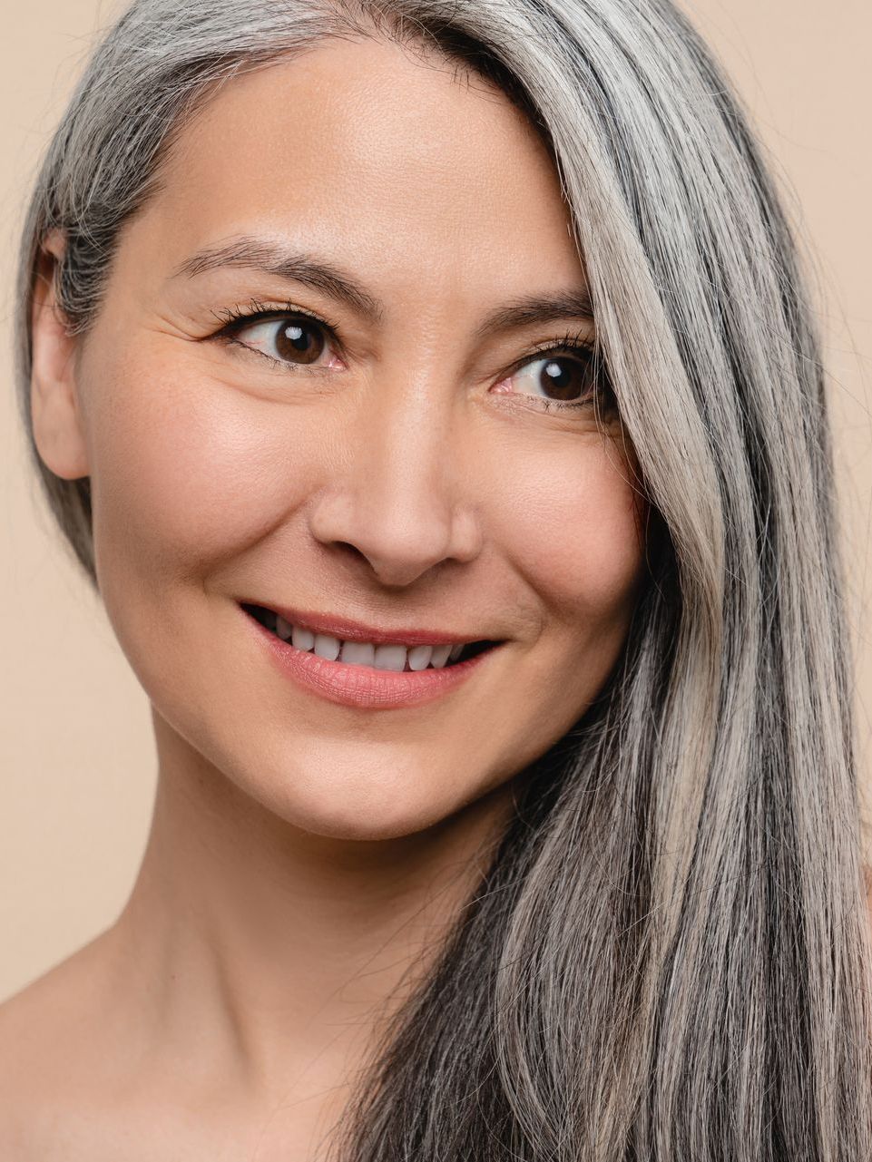 Woman with long gray and dark hair smiles, looking off to the side.