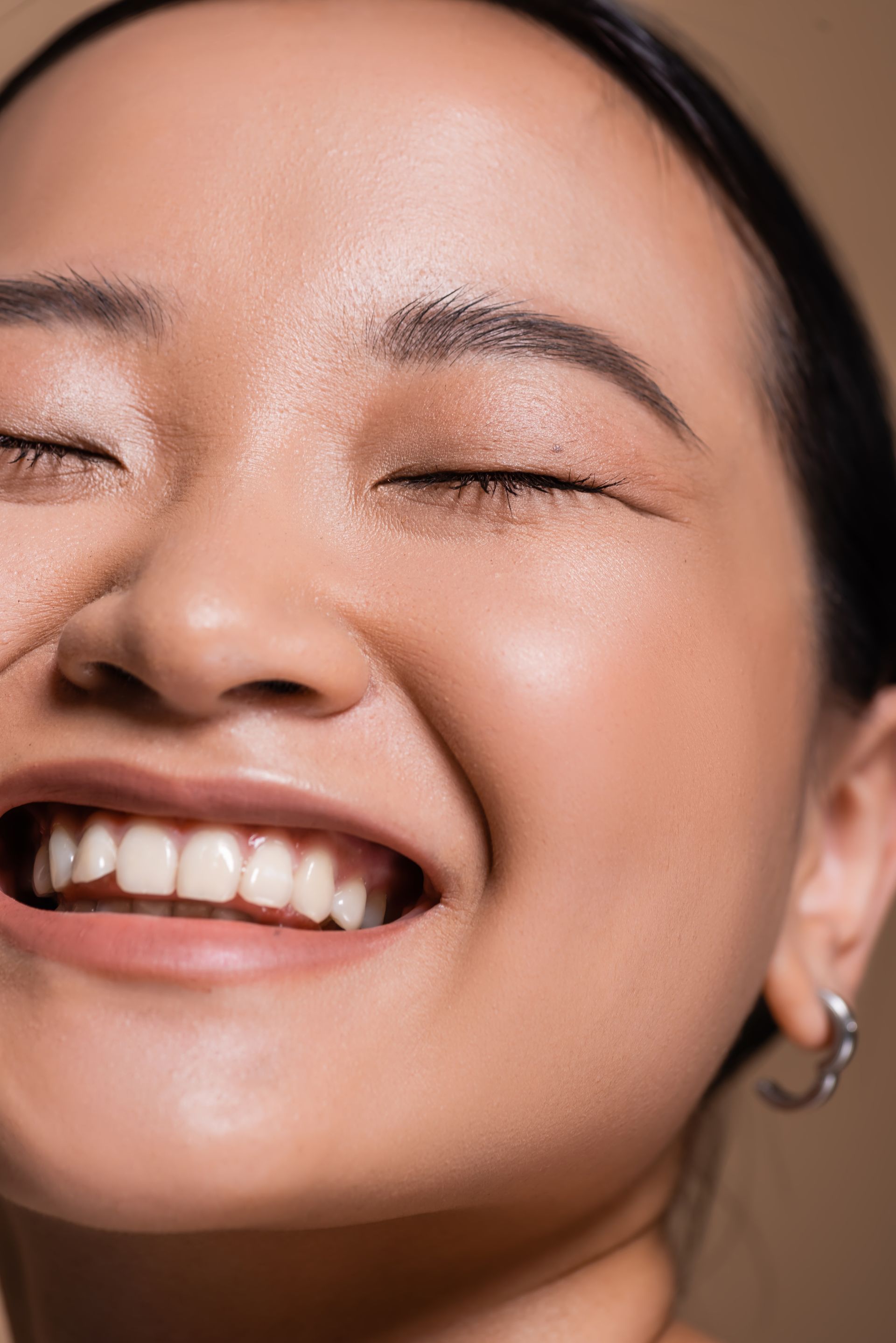 Smiling person with eyes closed, fair skin, dark hair pulled back, and silver hoop earring.