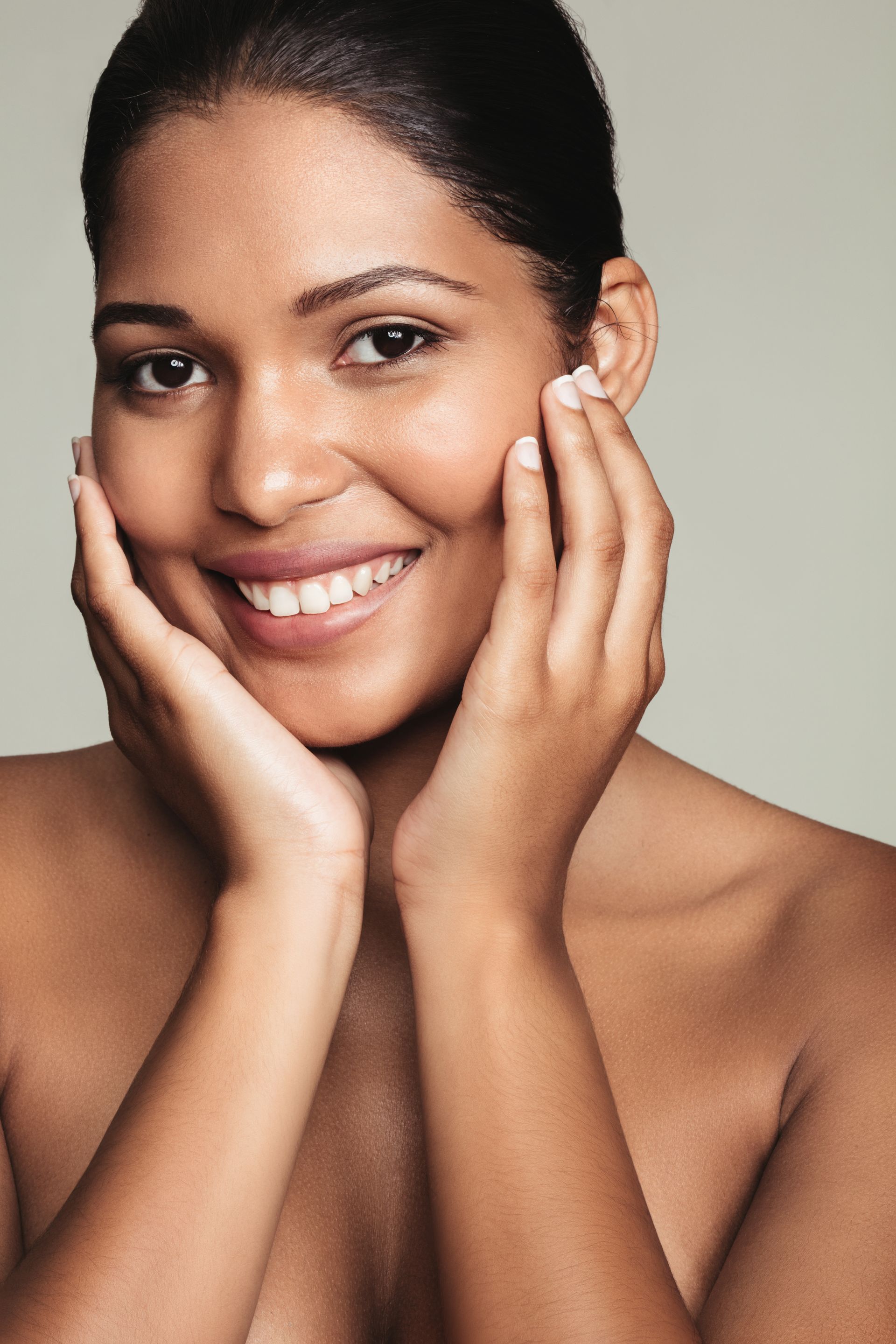 Woman with dark skin smiling, cupping her face.