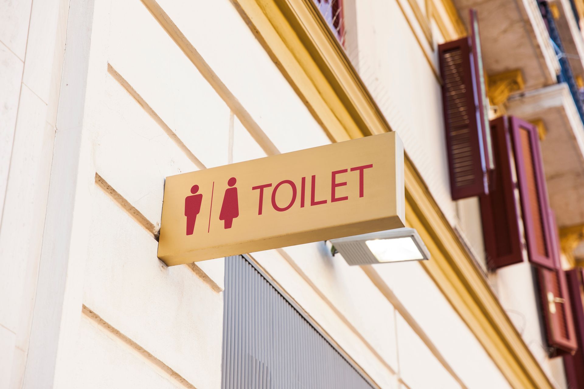 Toilet sign with male and female symbols, red on tan, mounted on a building.