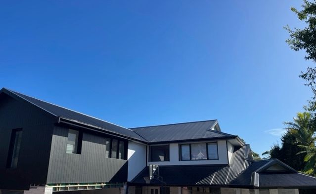 A Large House With a Black Roof and a Blue Sky in the Background — SRV Roofing in Coolum Beach, QLD