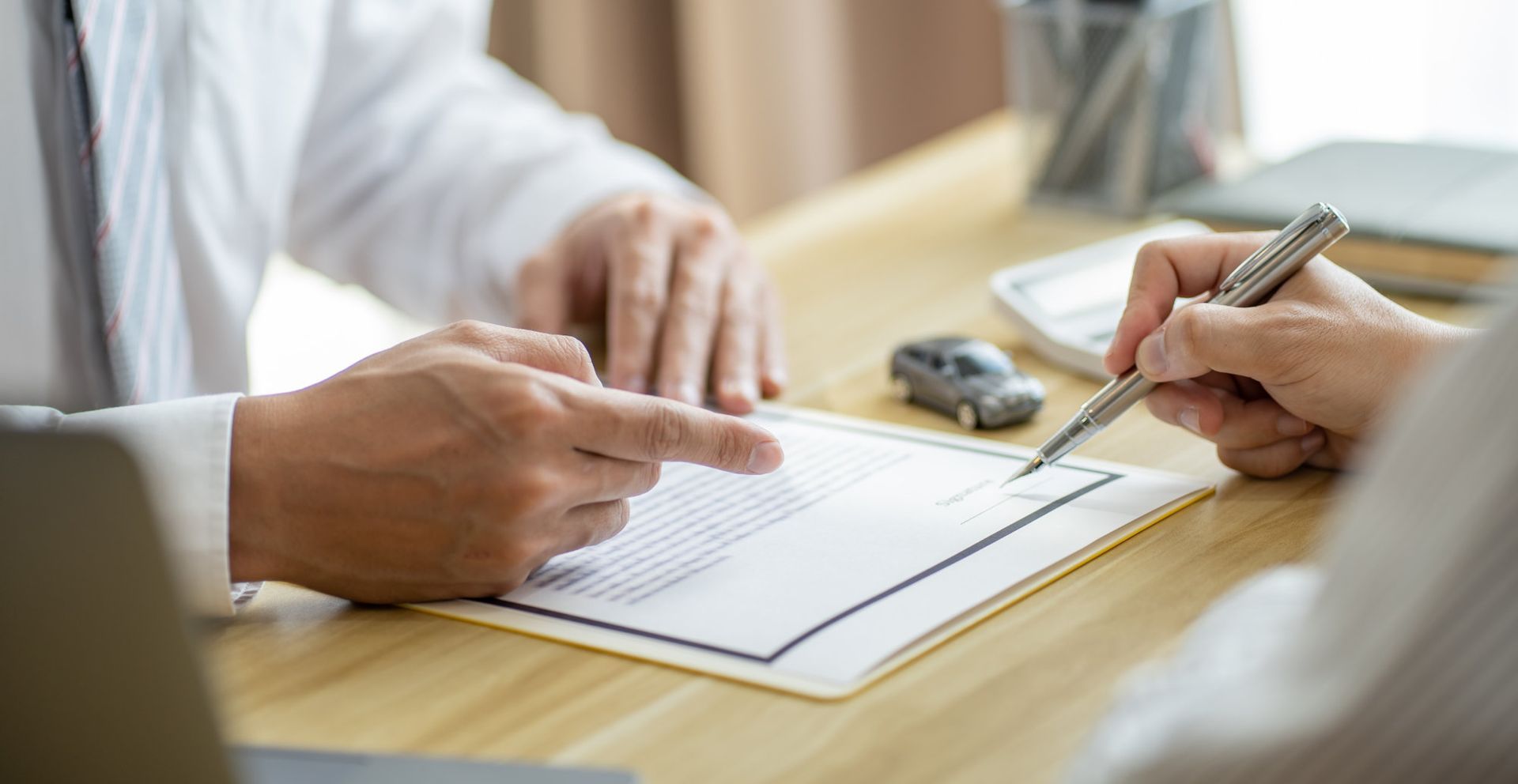 Deux personnes signant un document à un bureau, avec un stylo et un porte-bloc.