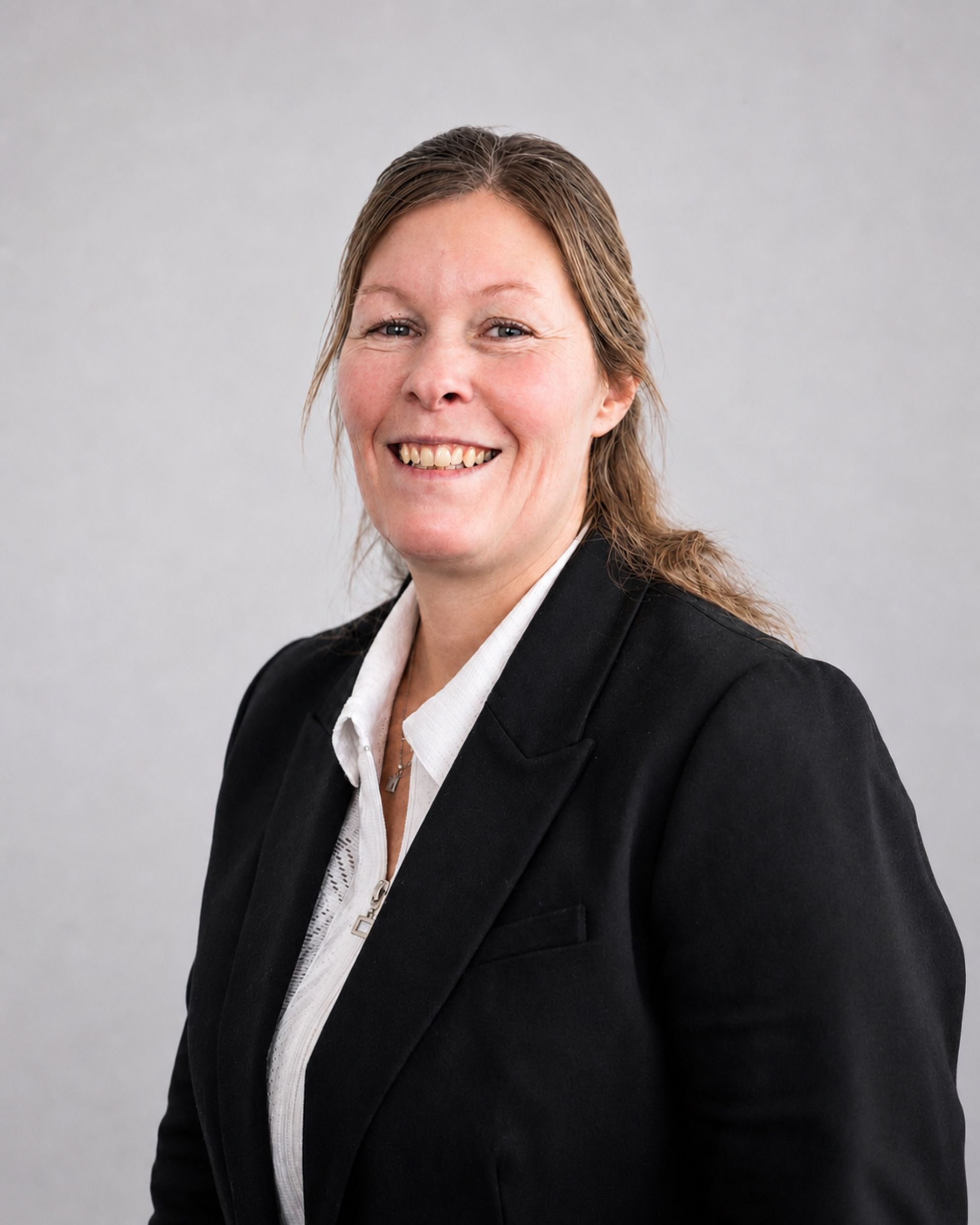 Femme souriante en blazer noir et chemise blanche sur fond gris clair
