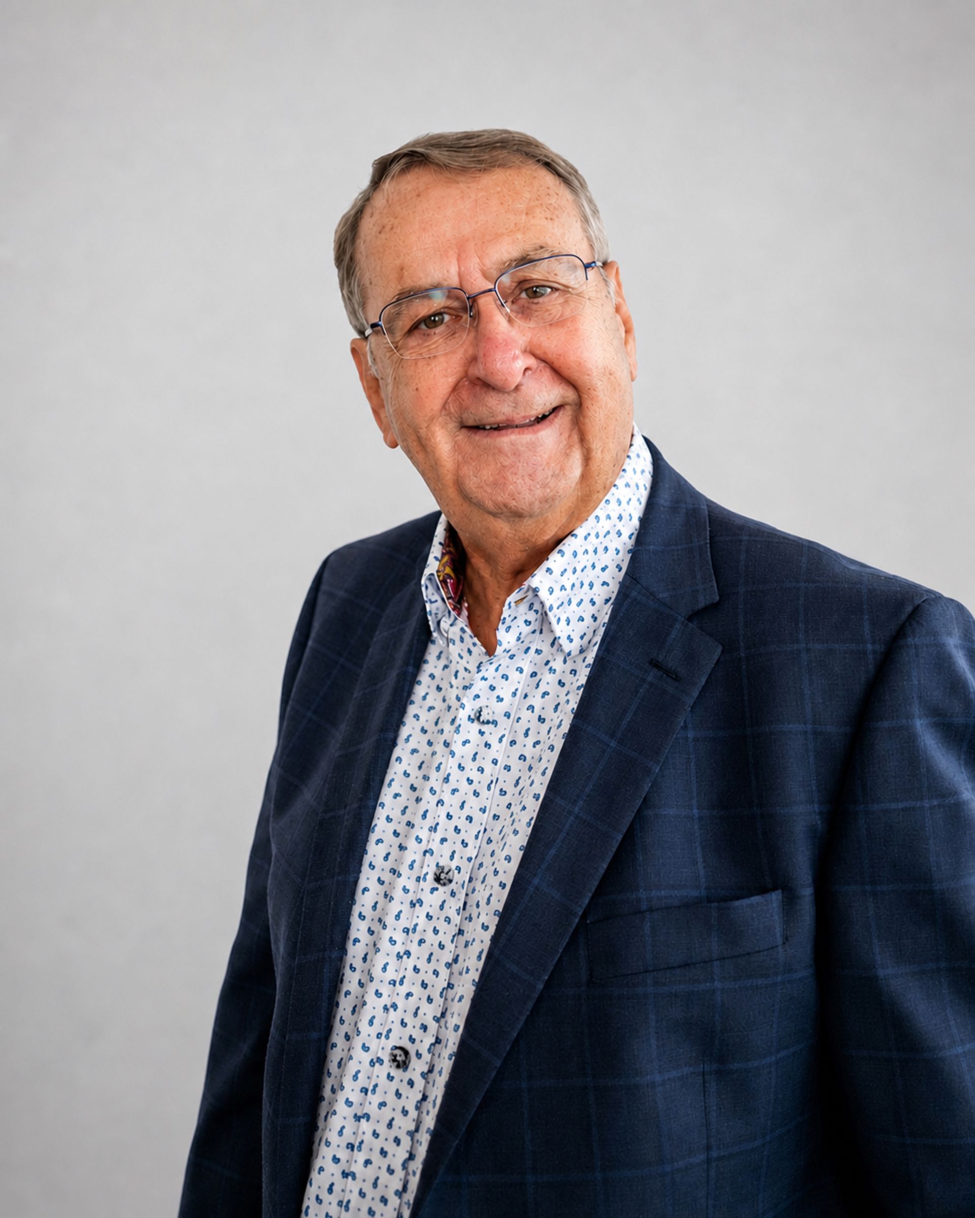 Portrait d’un homme souriant en blazer bleu marine et chemise à motifs, sur fond gris clair