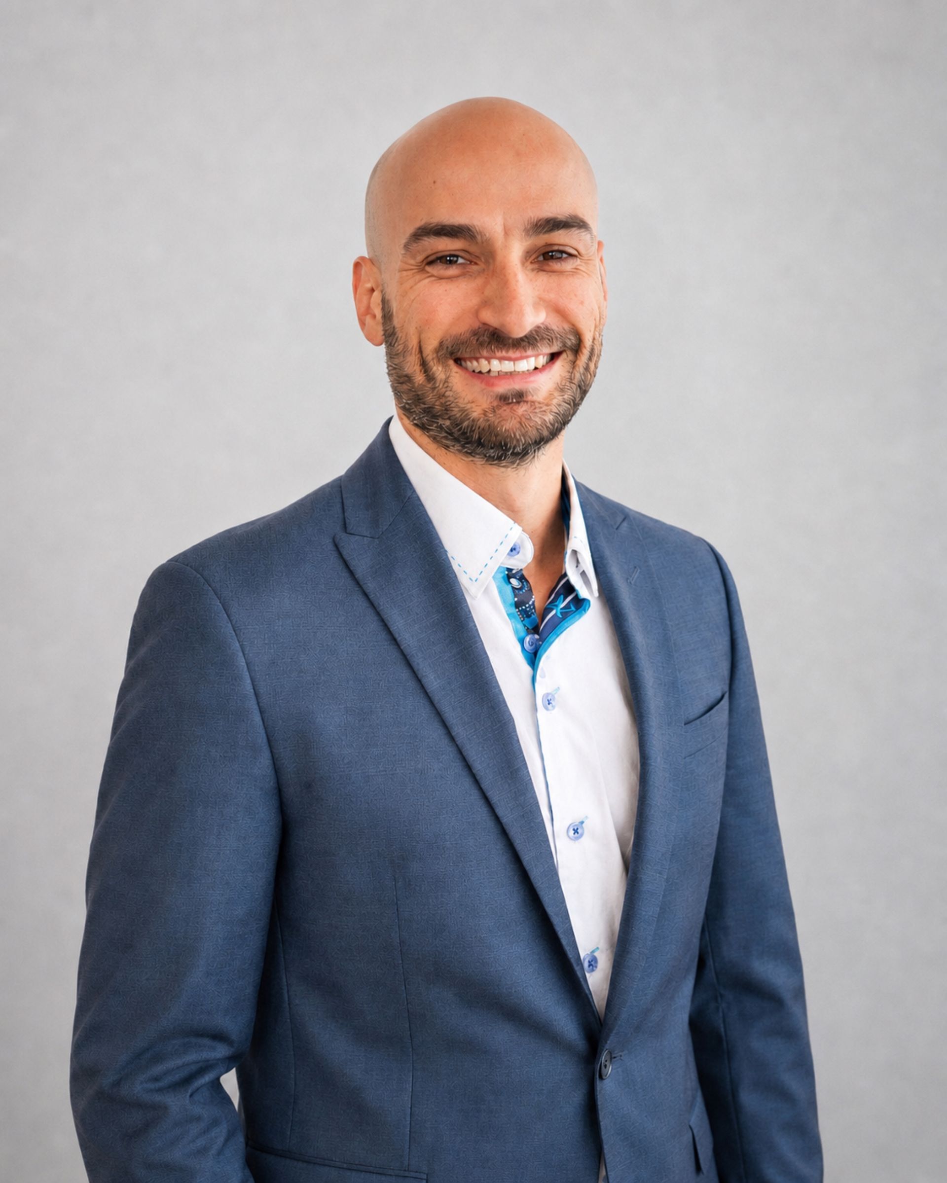 Homme souriant en veste de costume bleue et chemise blanche sur fond gris clair