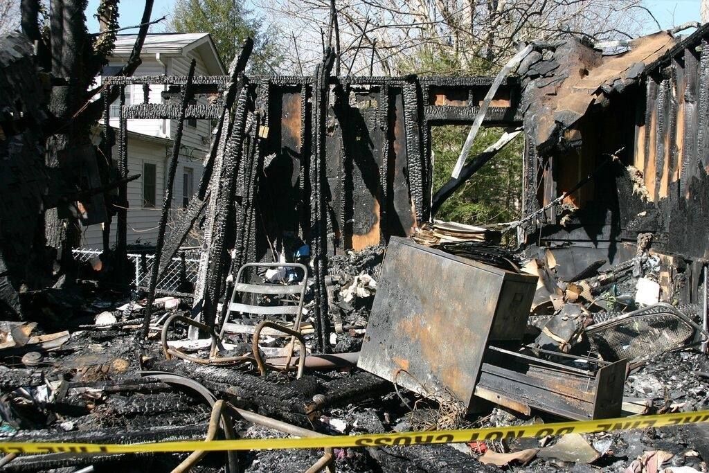 Vestiges calcinés d’un bâtiment incendié, aux murs effondrés et aux débris délimités par du ruban de sécurité