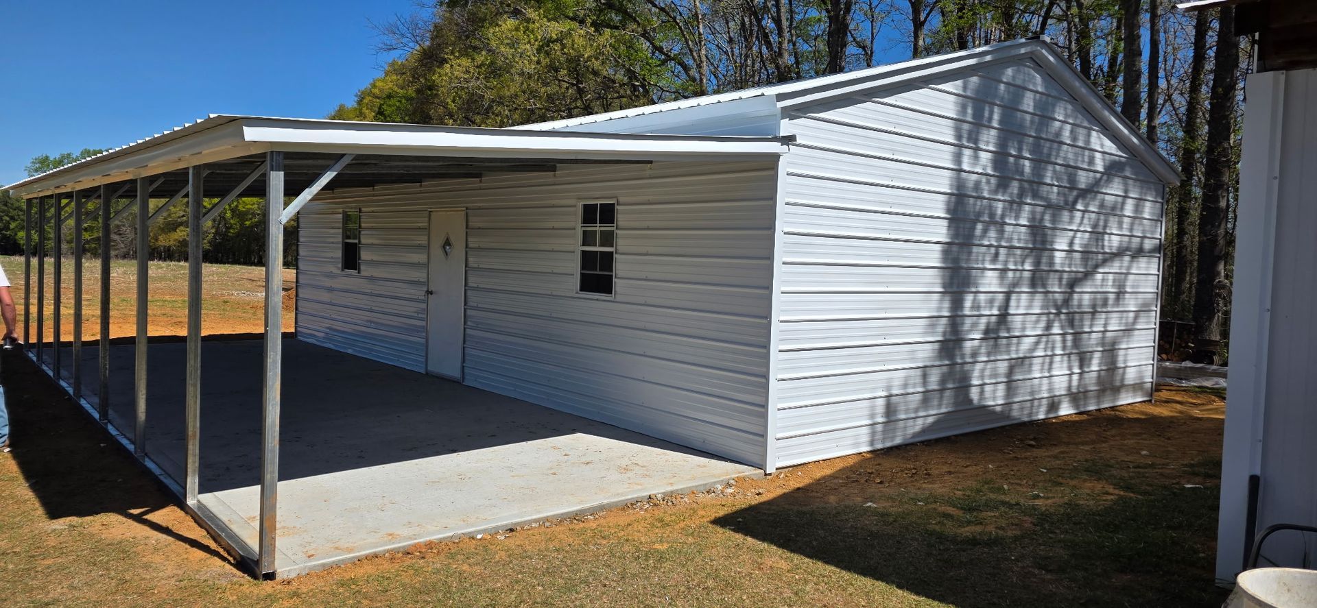 White house with a covered concrete porch and metal posts, set beside a grassy yard and trees.