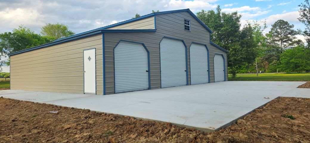 Tan metal warehouse with roll-up doors and a concrete pad in a grassy, open lot