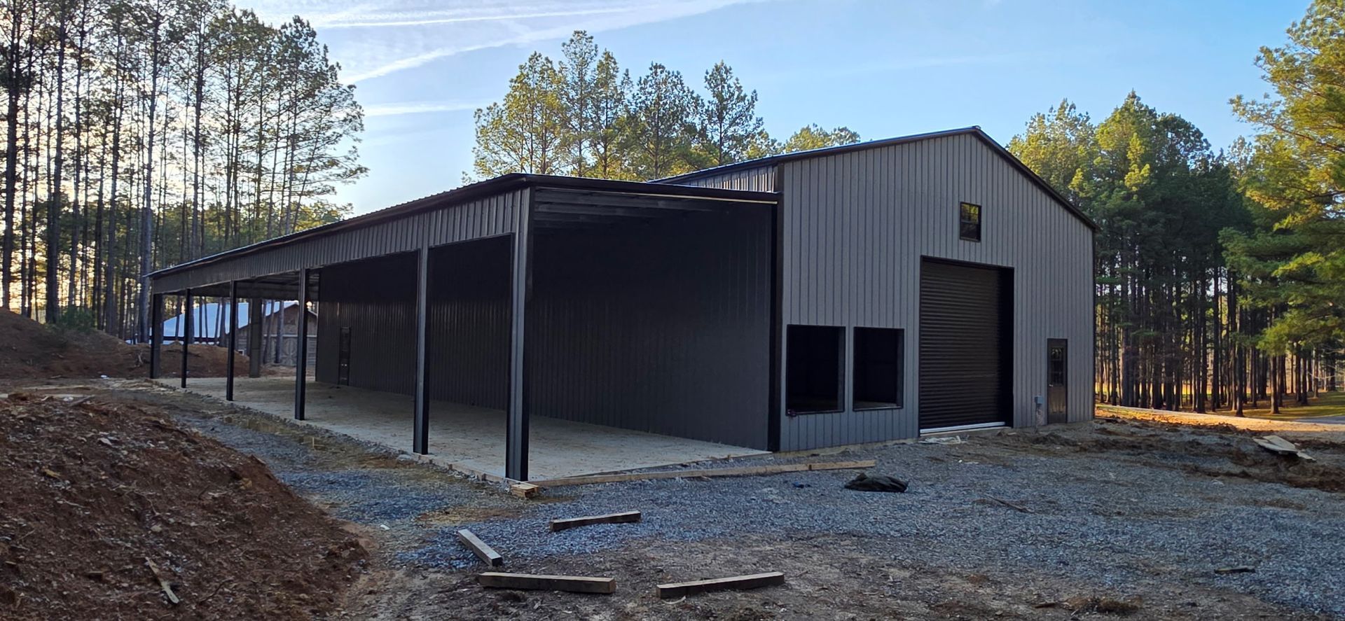 Large metal barn with a covered porch, set on gravel in a wooded rural area