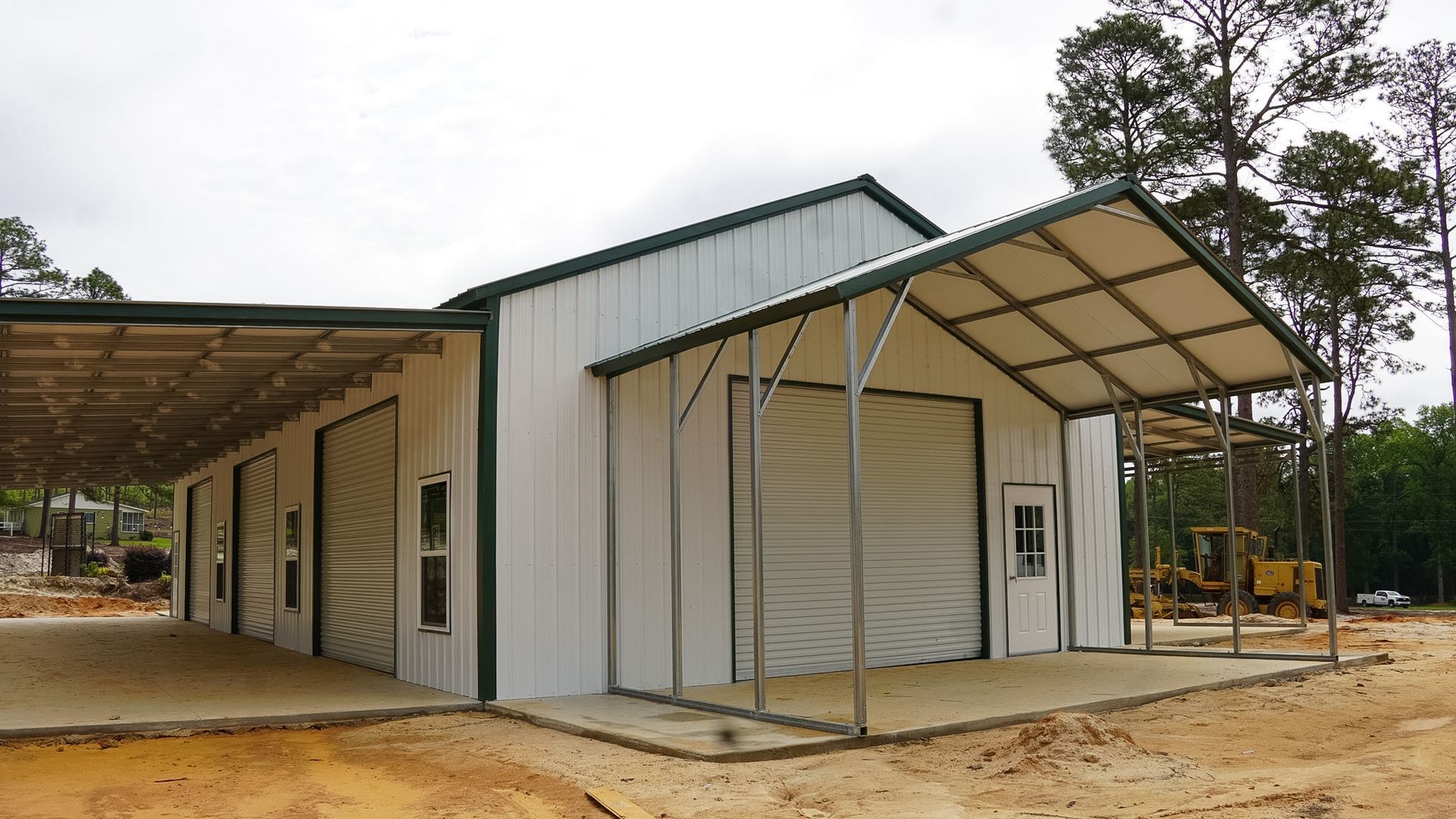 Small white metal building with a covered front entrance on a dirt lot in a wooded area