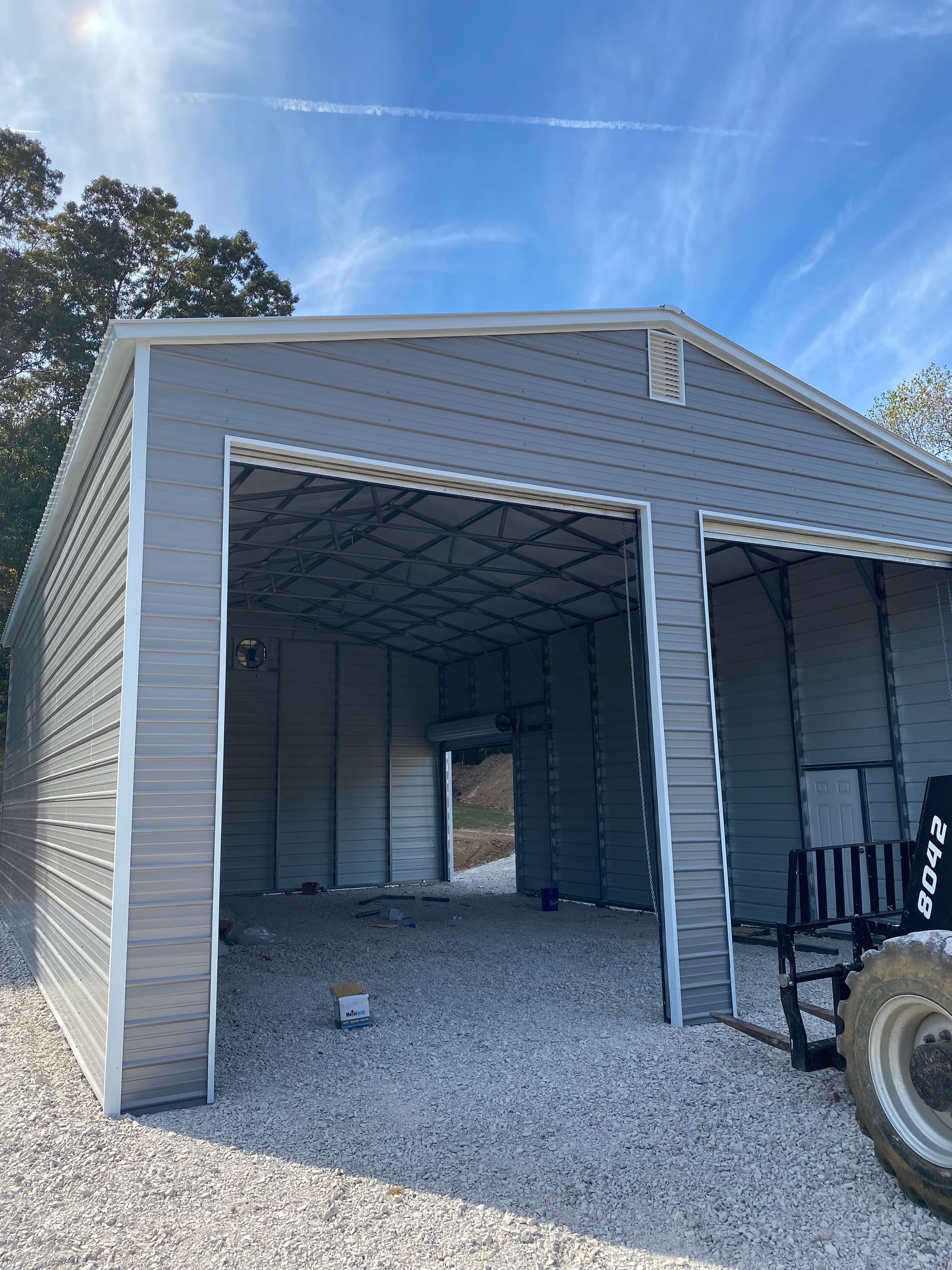 Open garage with gravel floor, gray siding, and a tire visible at the right edge under a blue sky