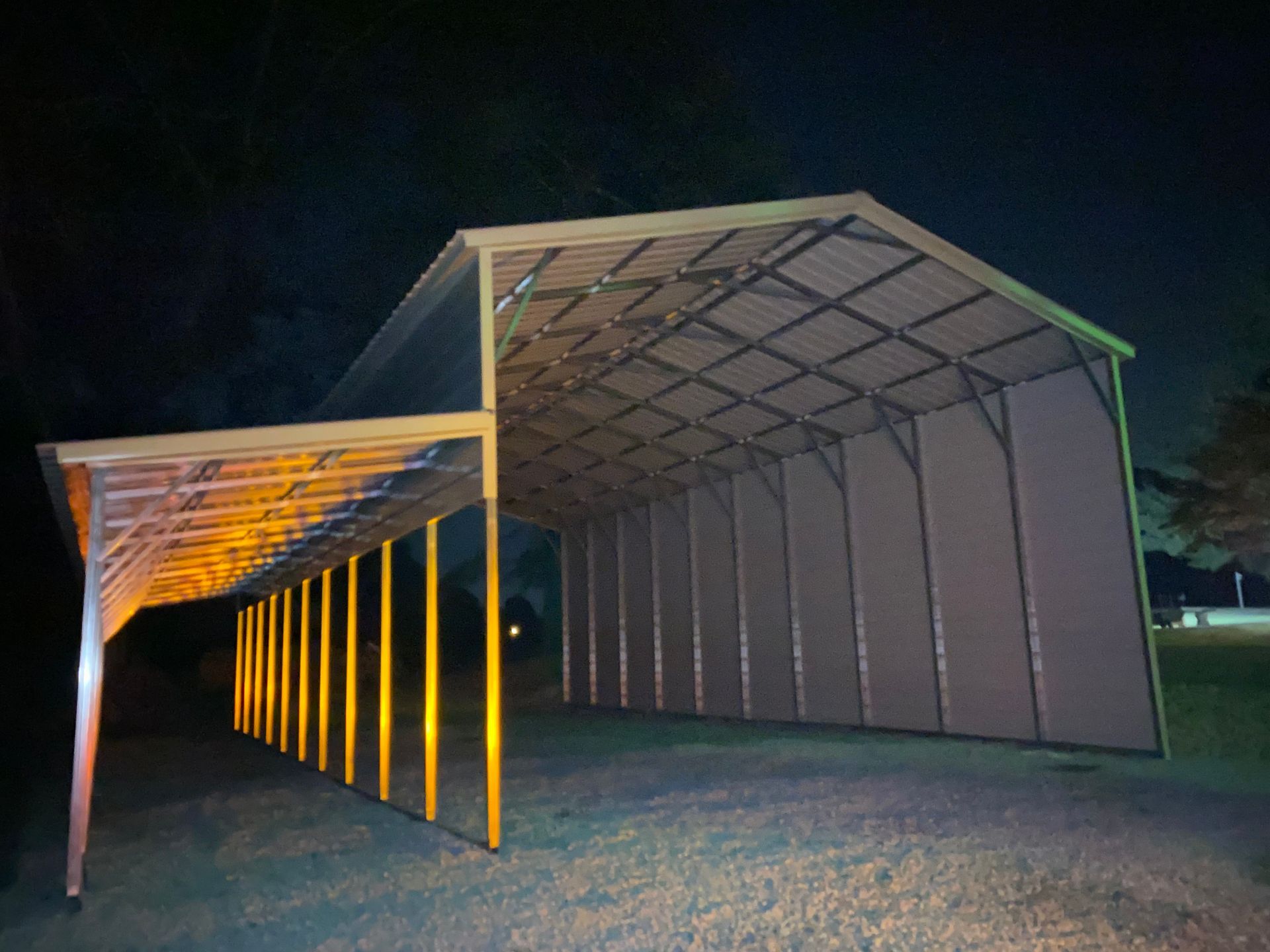 Night-lit geometric pavilion with orange posts and a slanted roof on grass.