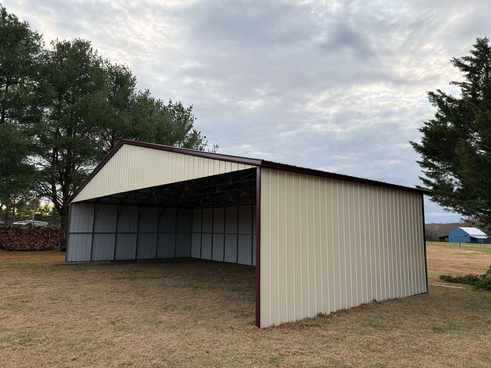 Open-sided metal shed in a grassy field under a cloudy sky