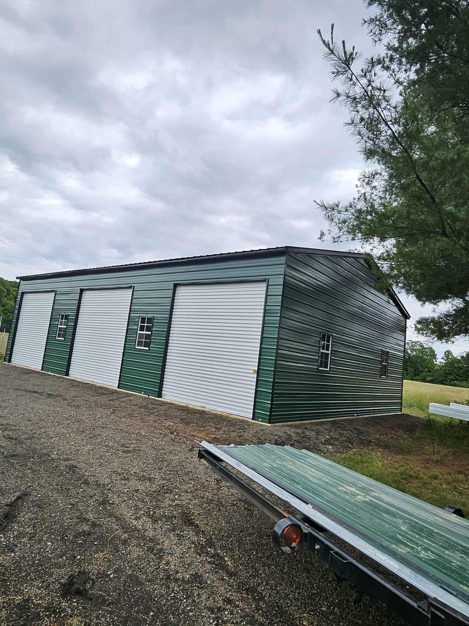 Green-and-white storage shed with roll-up doors on a gravel lot under a cloudy sky