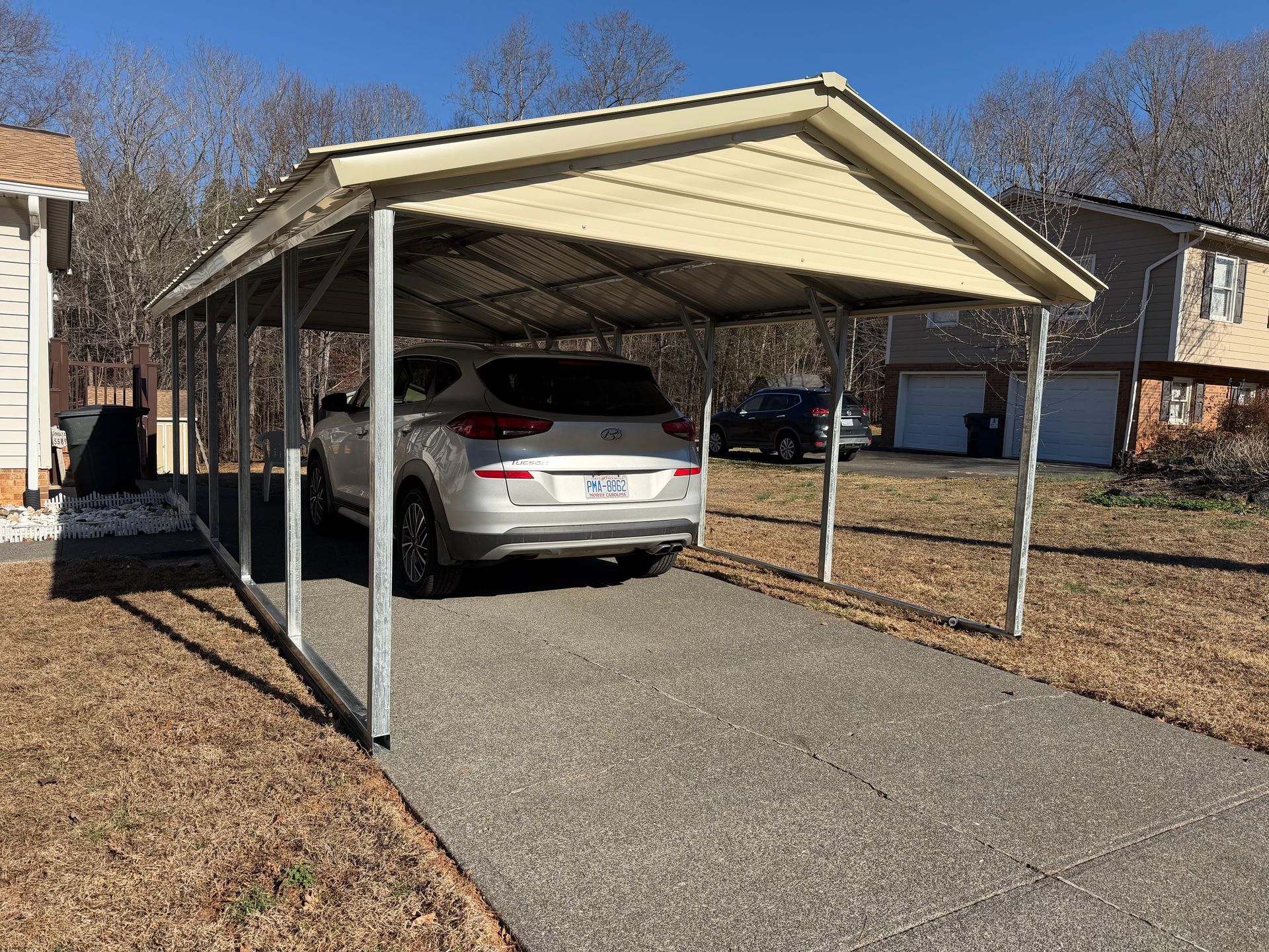 White sedan parked under a beige carport beside a driveway in a suburban neighborhood