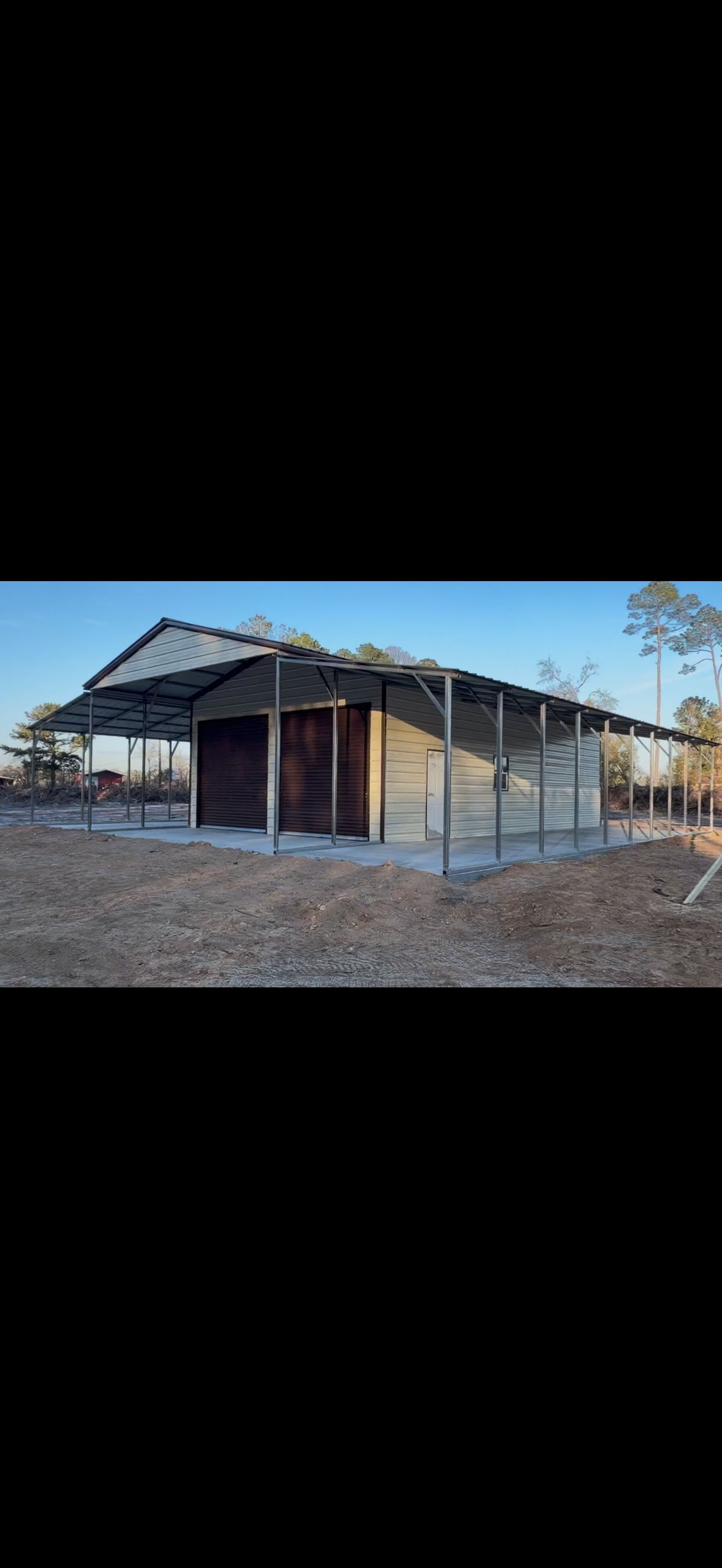 Partially built house frame with corrugated metal roof in a dry, open lot at sunset
