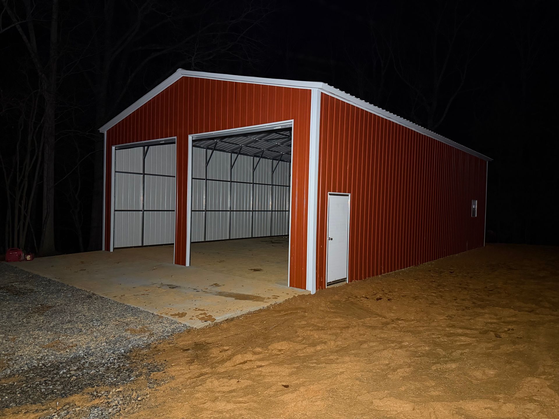 Red metal open-sided barn at night with concrete floor and dirt foreground.