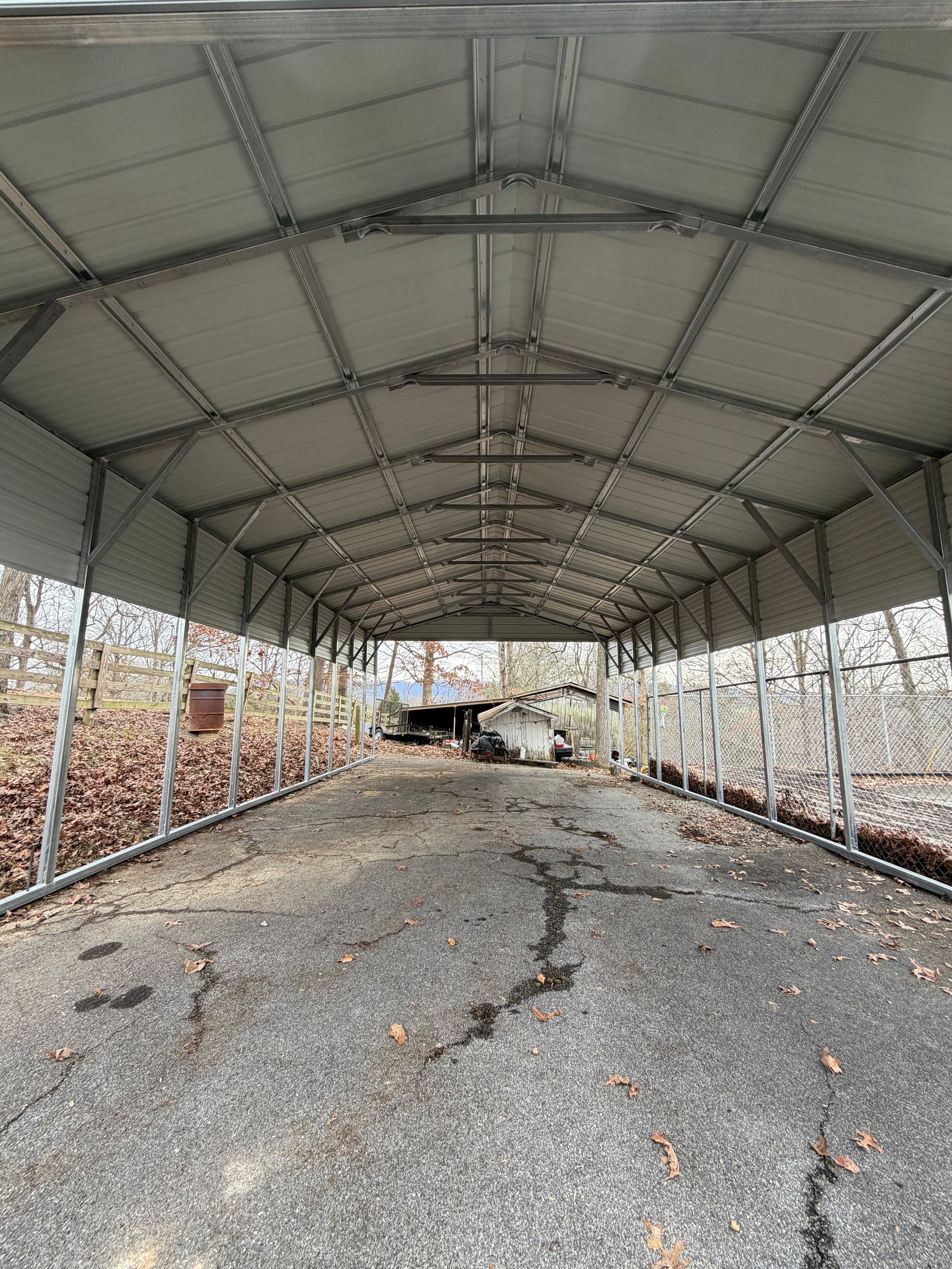 Empty metal-roofed shed with gravel floor and open sides, viewed down the center aisle.