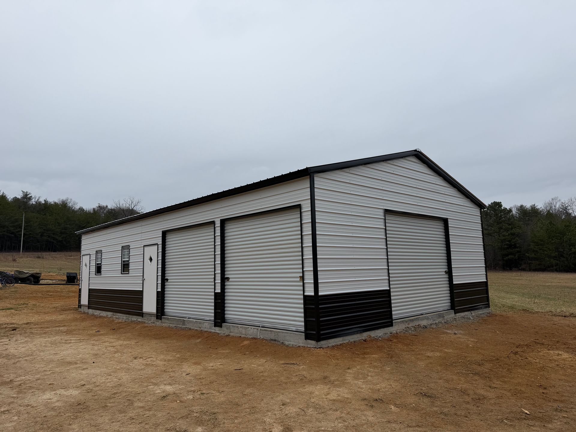 White metal garage building with multiple roll-up doors on a gravel lot under cloudy sky