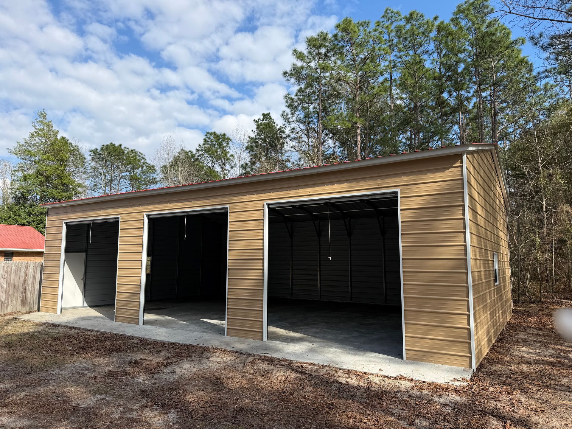 Three-bay wooden garage with open doorways in a wooded yard under a blue sky