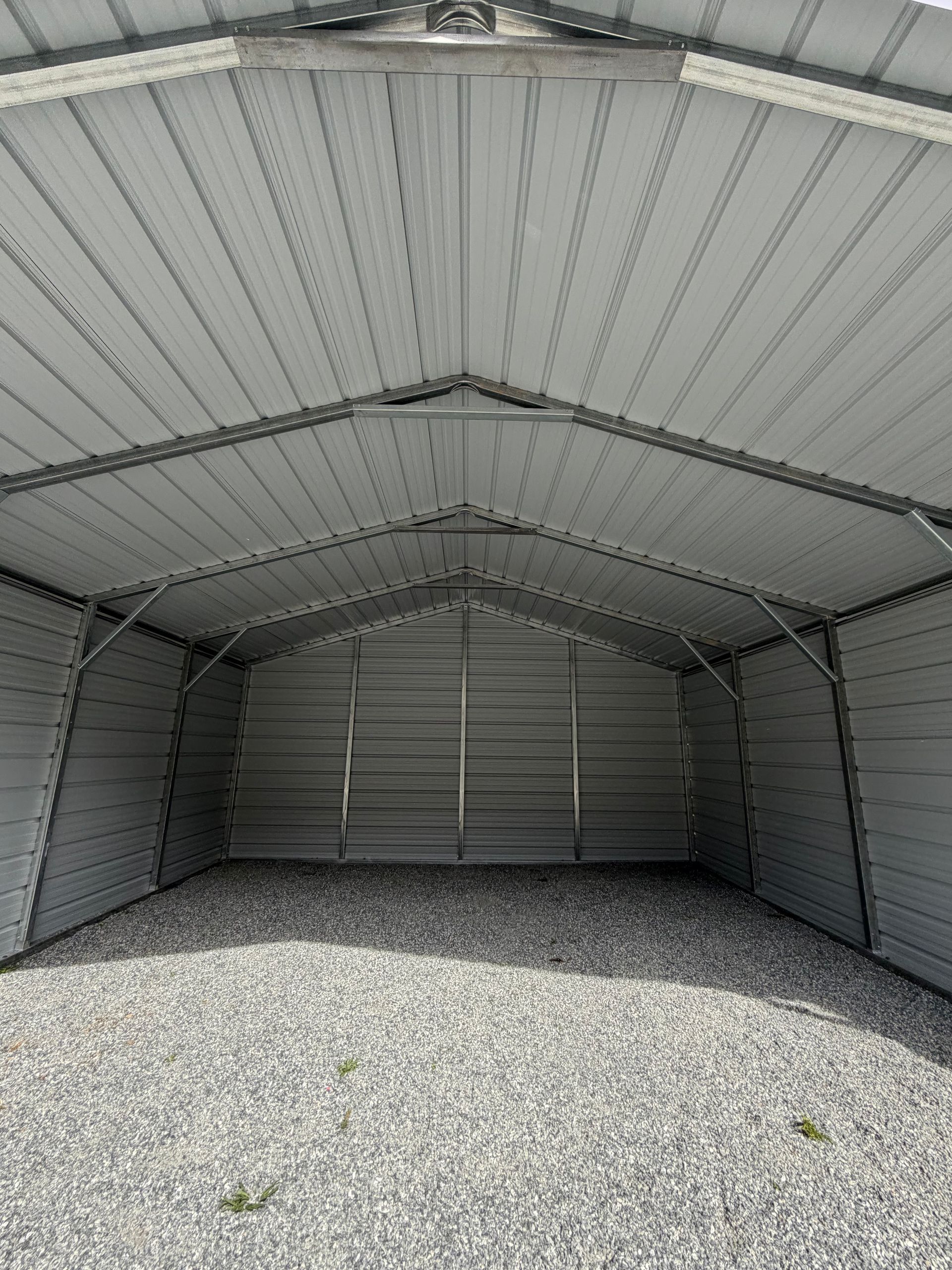 Empty gray metal storage shed with gravel floor and open front view