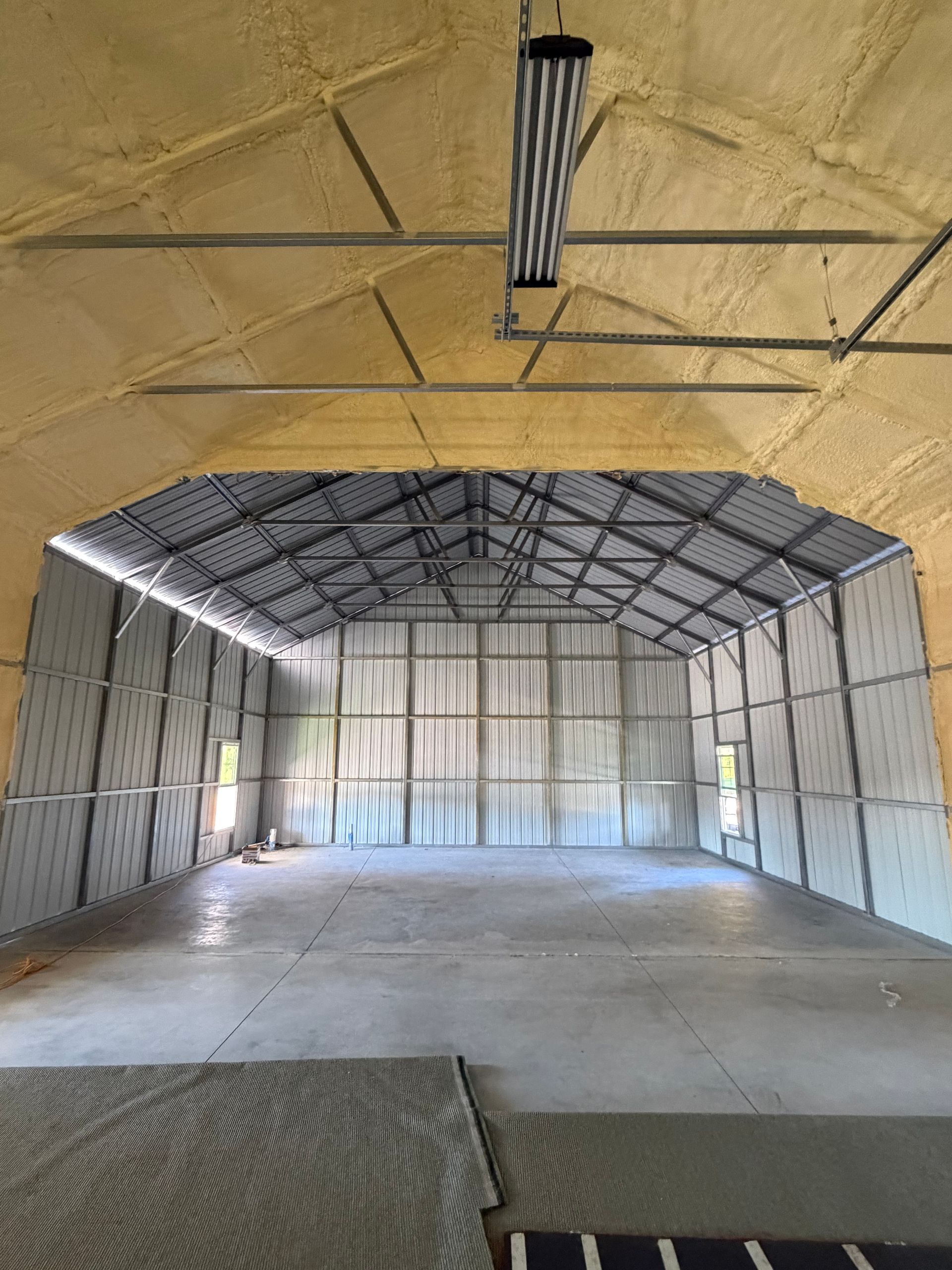 Empty unfinished warehouse interior with metal-framed walls, exposed roof trusses, and concrete floor