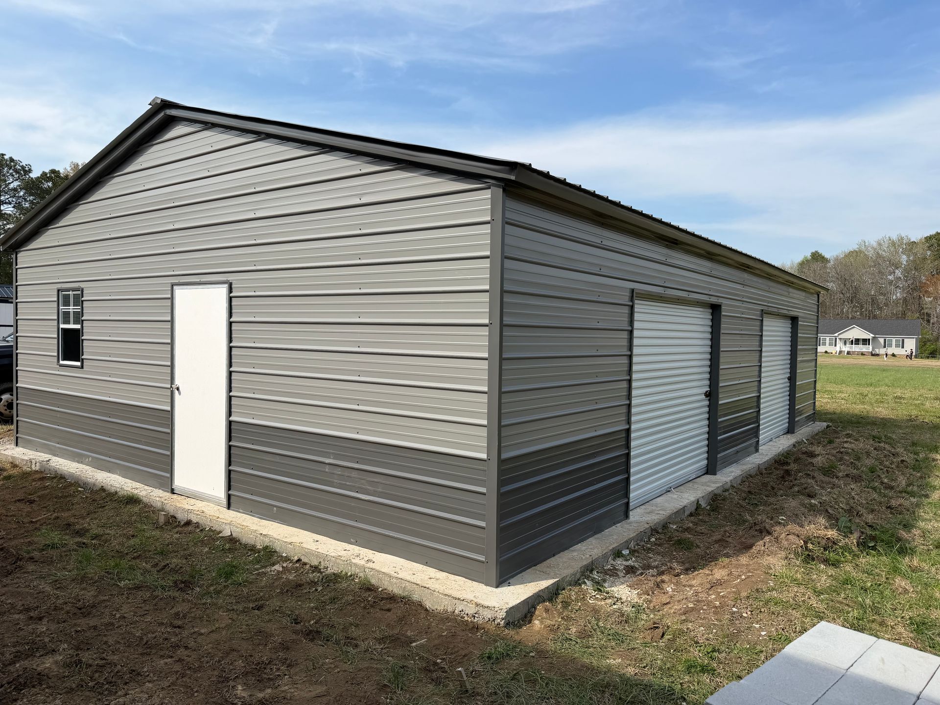 Gray metal storage building with white doors and garage-style bays on a grassy lot