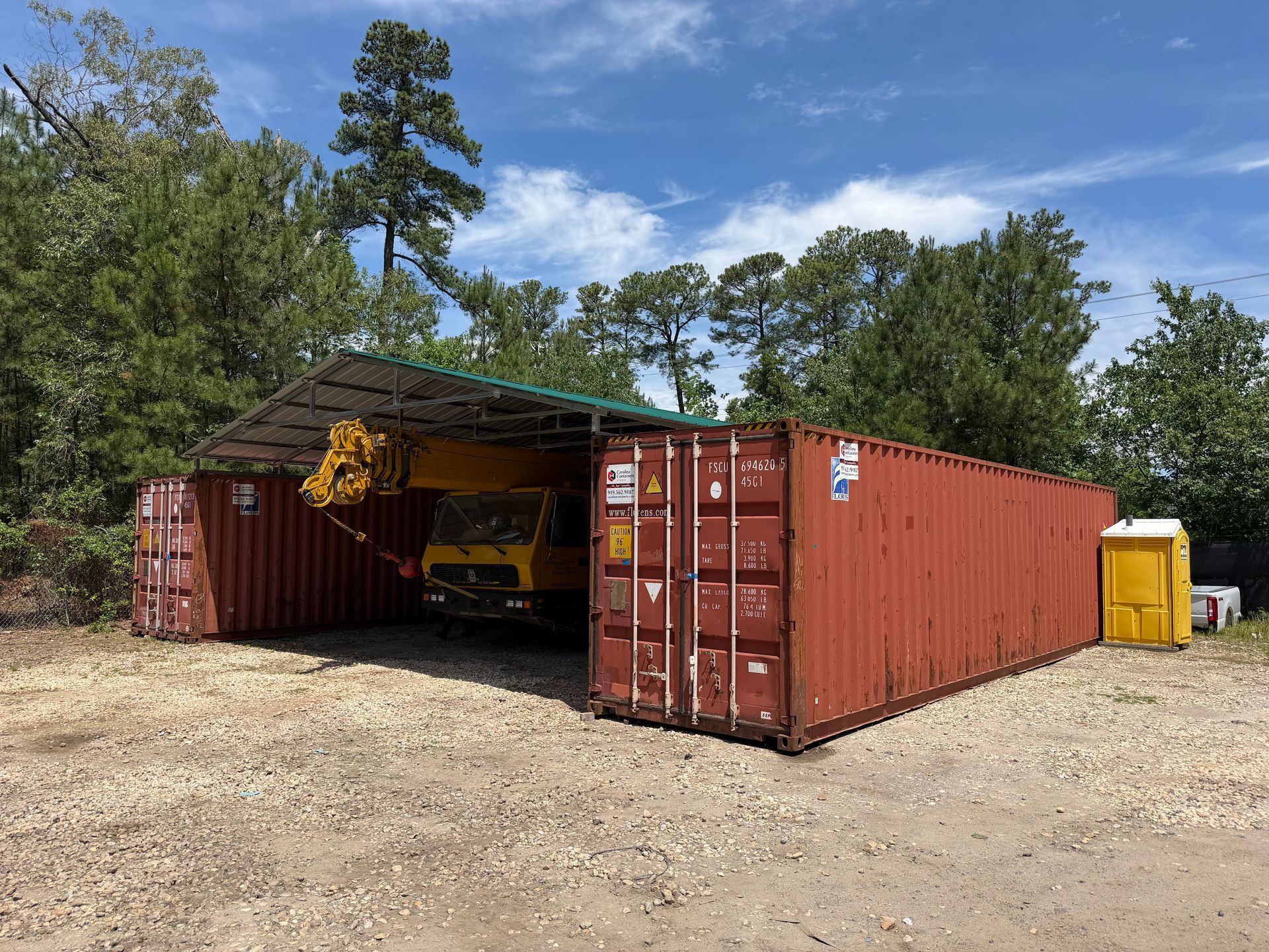 Red shipping containers used as a storage shed, with a yellow machine inside and trees in the background