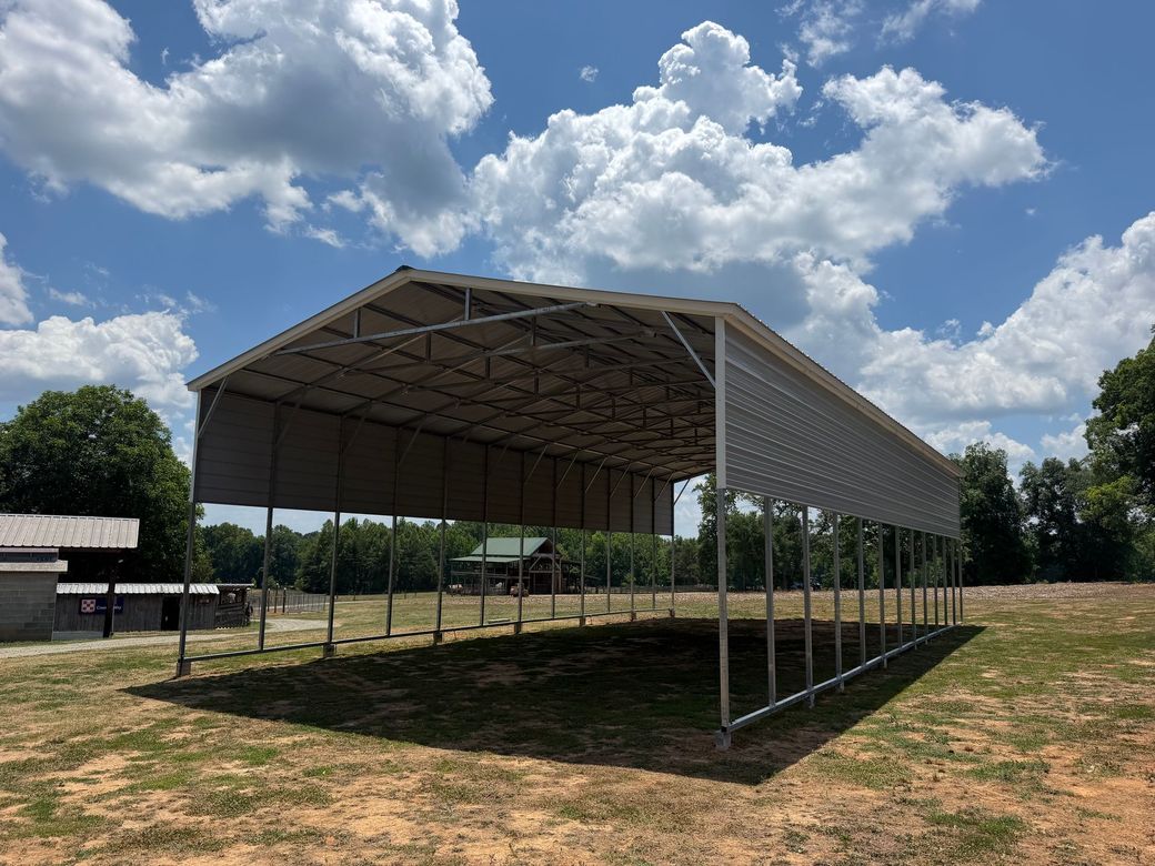 Open-sided metal pavilion on a grassy field under a cloudy blue sky