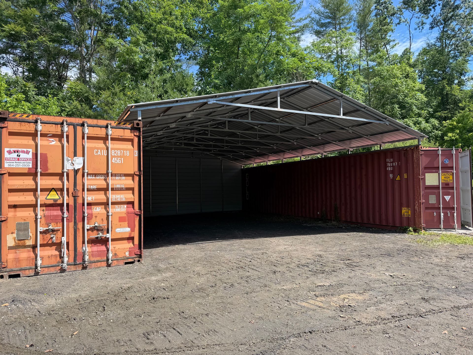 Open shipping container used as a makeshift shelter, with orange and red containers in a gravel lot.