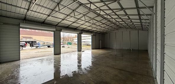 Empty metal warehouse with open garage doors and wet concrete floor reflecting light