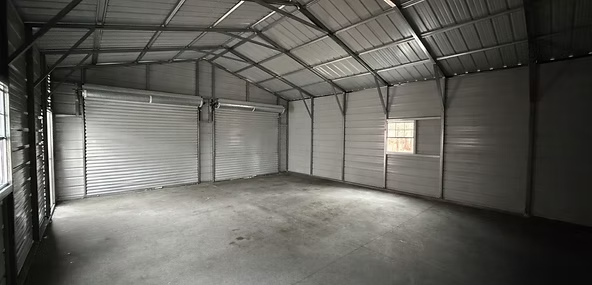 Empty metal storage shed with corrugated walls and concrete floor, lit by a small window