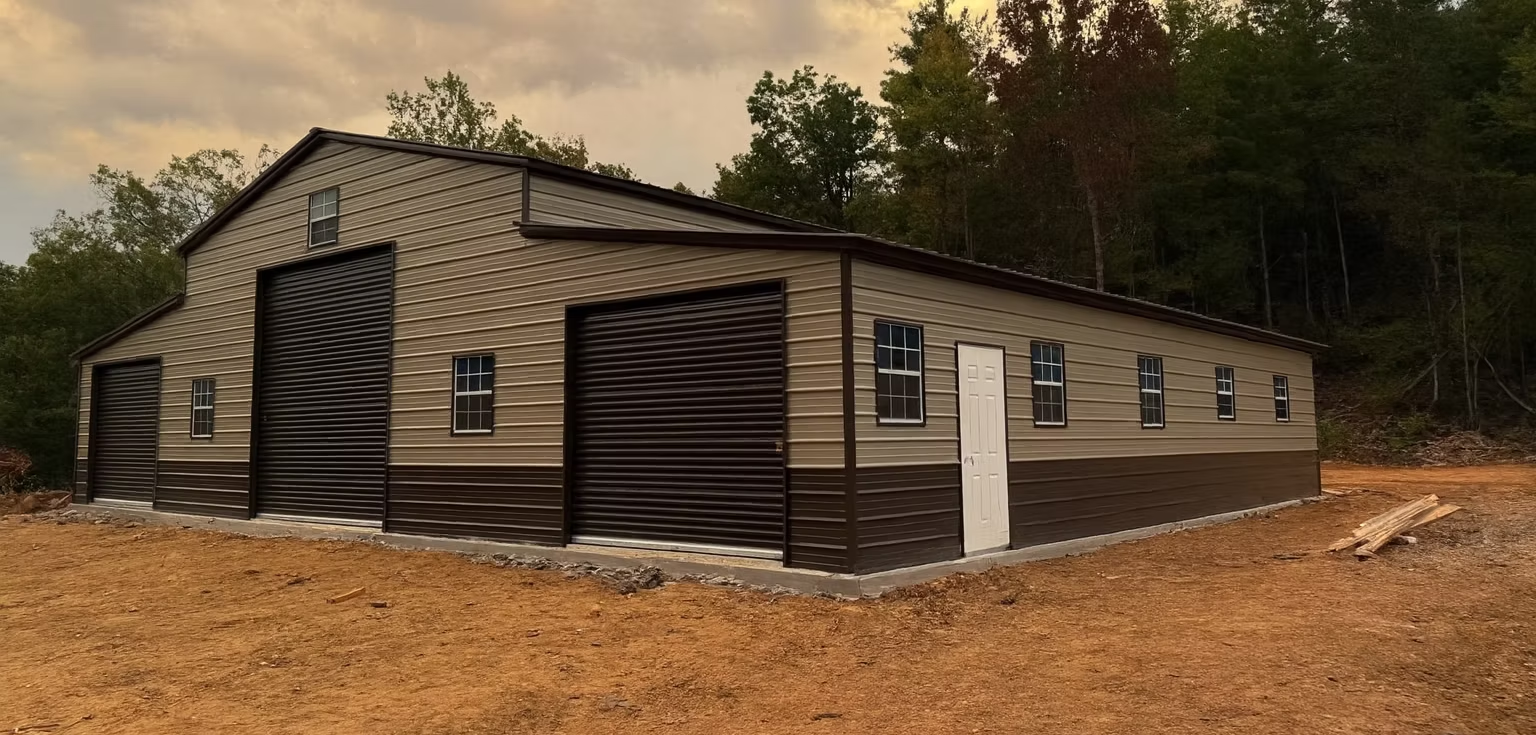 Single-story beige building with dark siding in a wooded area, surrounded by dirt ground.