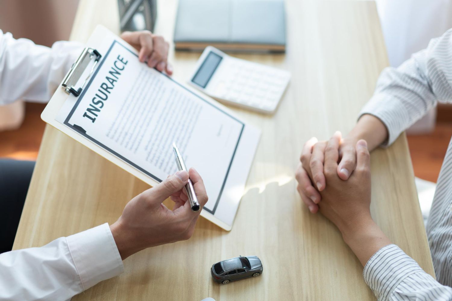 Person showing insurance policy to another; car model on table.