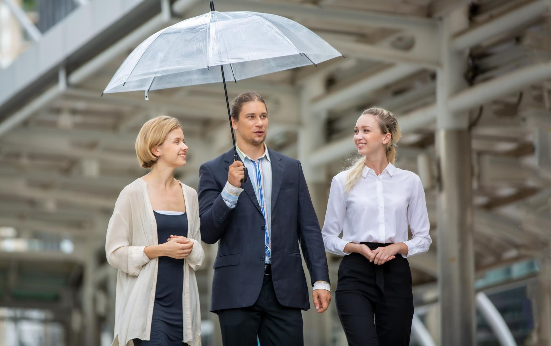 Three people walking under an umbrella outdoors. The man holds the umbrella, women on either side.