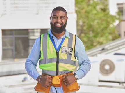 Construction worker wearing safety vest, smiling outdoors.