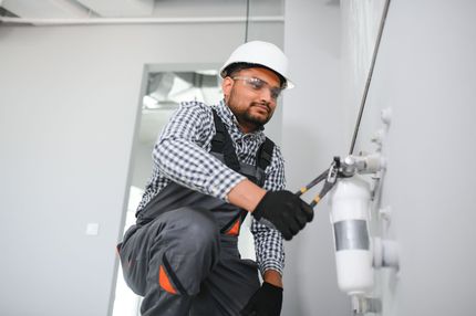 Construction worker in safety gear installing a water filter on a white wall.