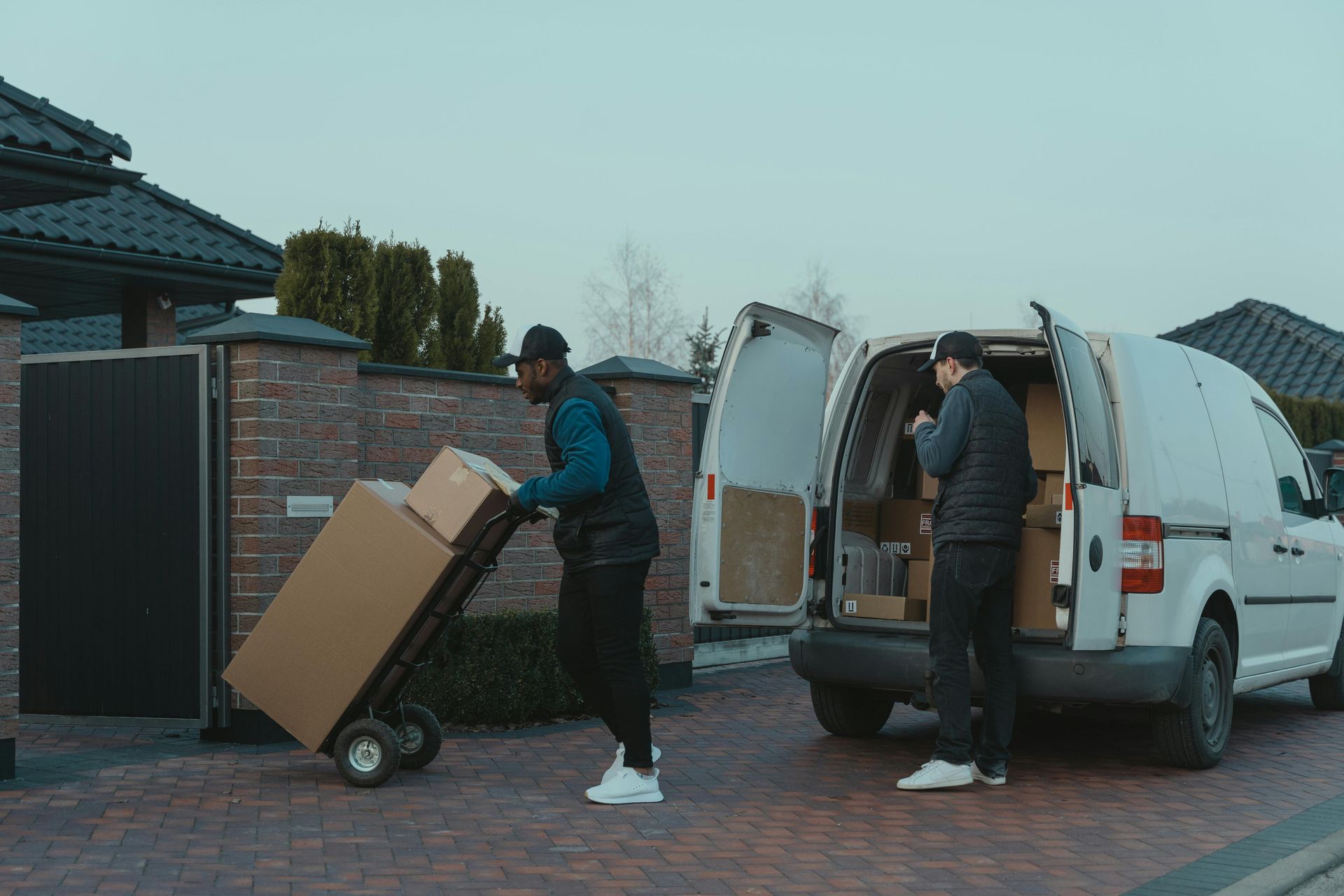 Two delivery workers unloading boxes from a van in front of a house.