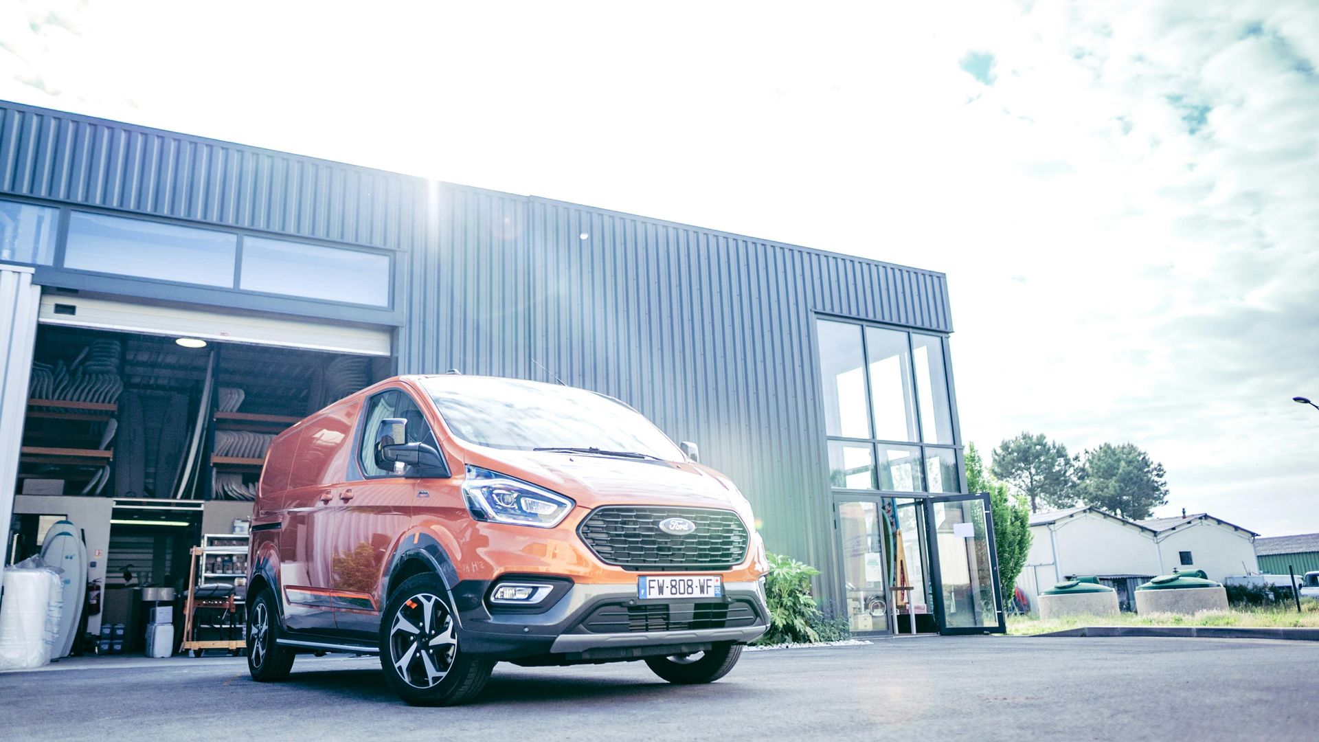 Orange and black cargo van parked outside a building with its door open under a bright sky.