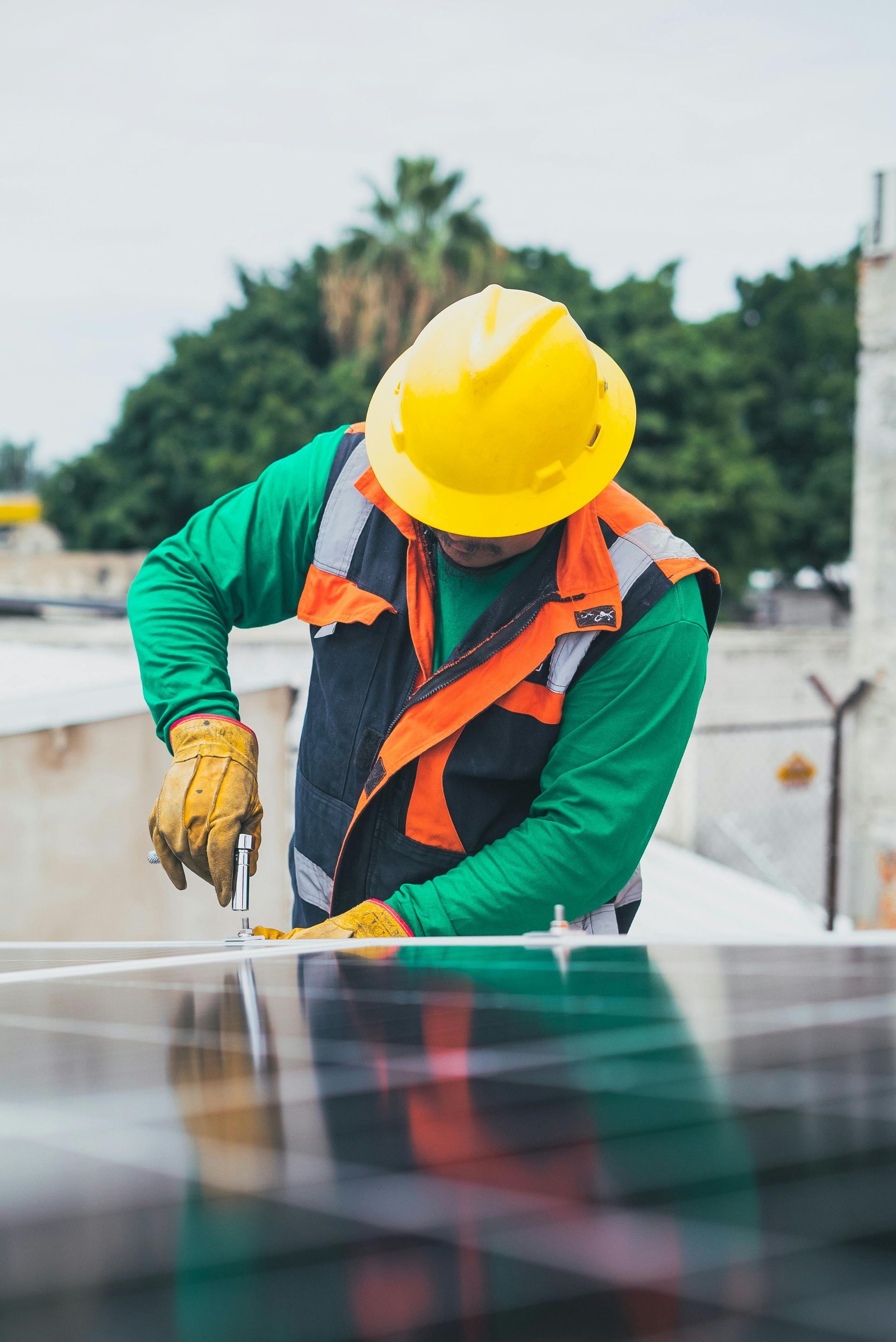 Construction worker in yellow hardhat, installs solar panel, wearing safety vest and gloves.